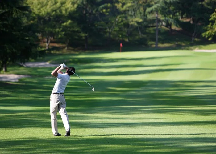 Person hitting a golf ball on a lush golf course with trees in the background.