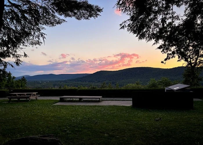 Sunset over a mountain range viewed from a park with benches and trees in the foreground.