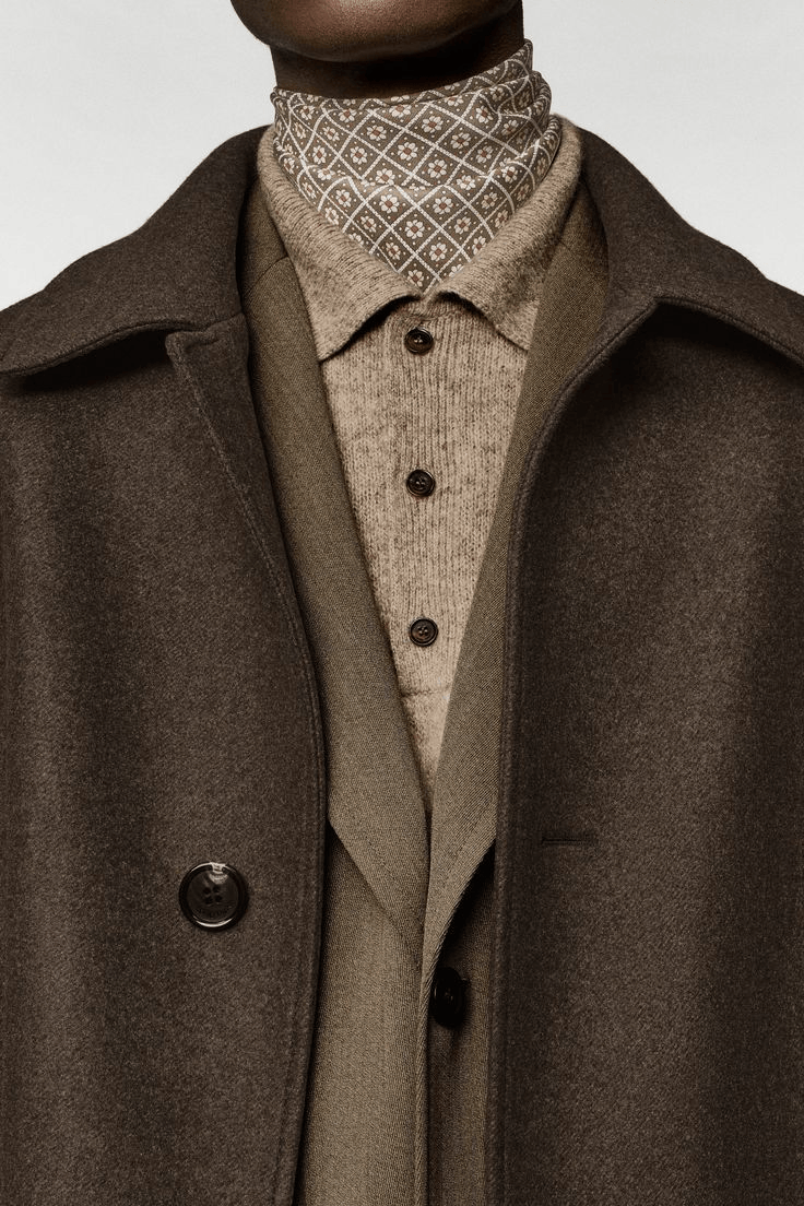 Close-up of a person's outfit featuring a patterned scarf, beige shirt, and a dark brown coat.
