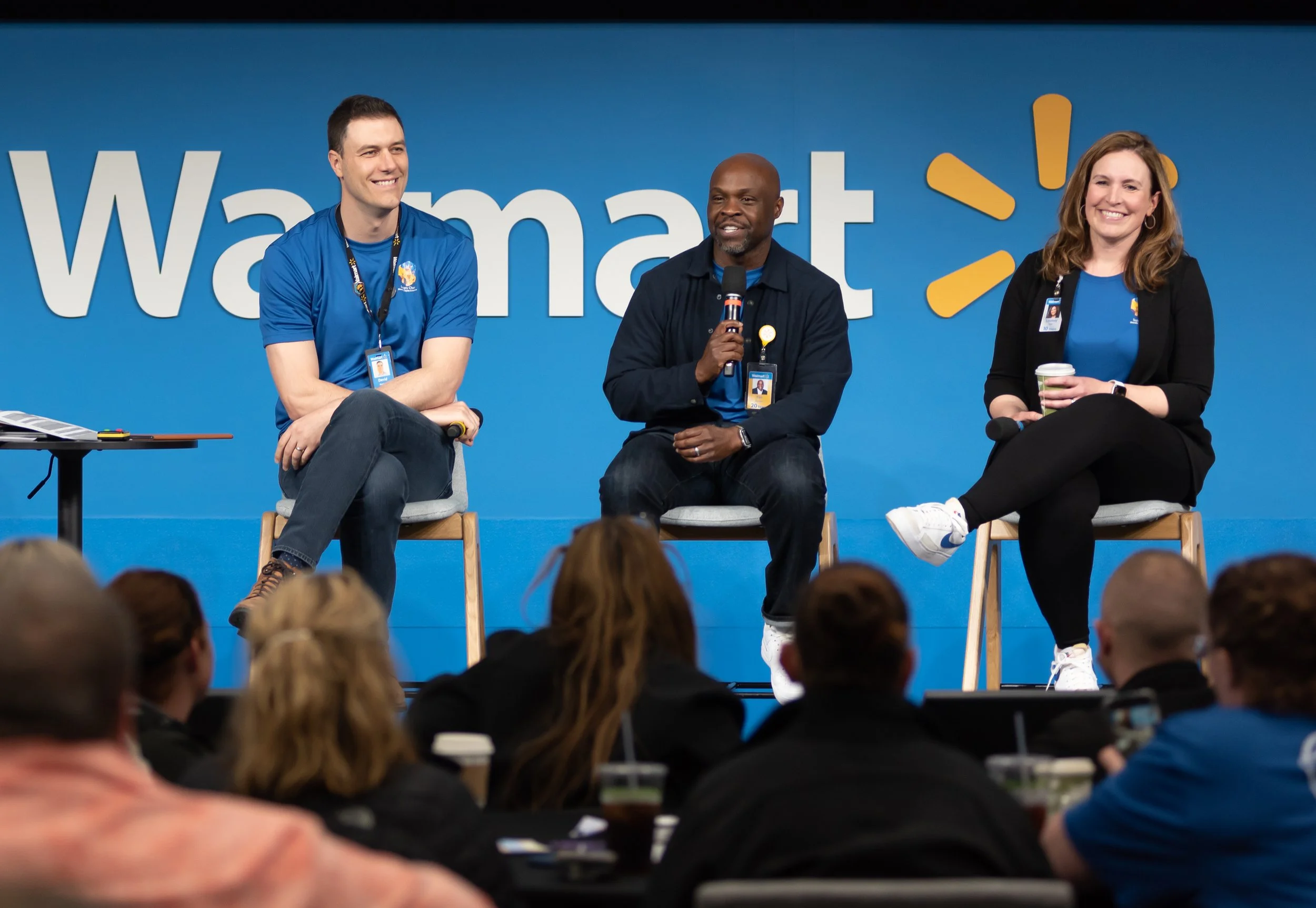 Three people sitting on a panel in front of a large Walmart logo, participating in a discussion during a Walmart event.