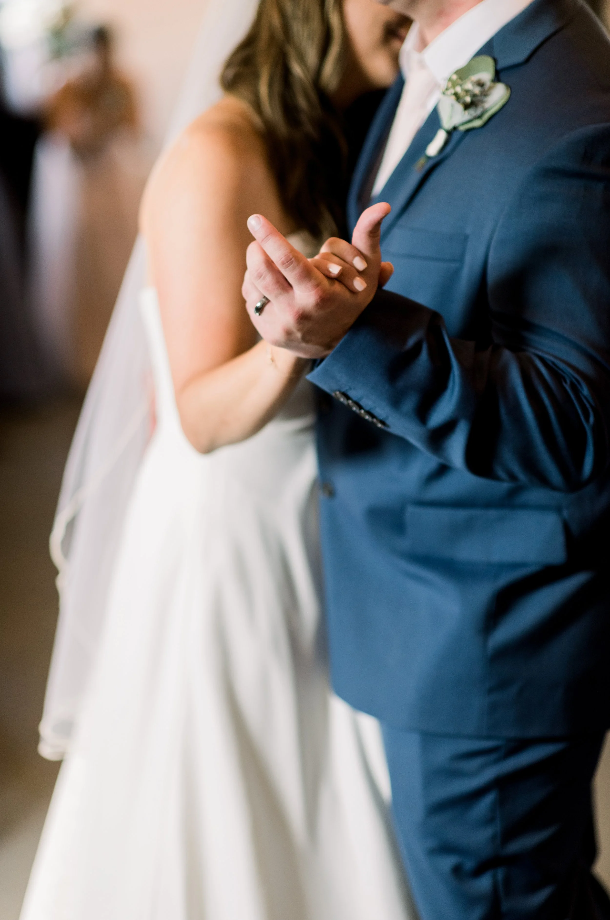 Close-up of a bride and groom dancing, focusing on their hands clasped together during their wedding dance.