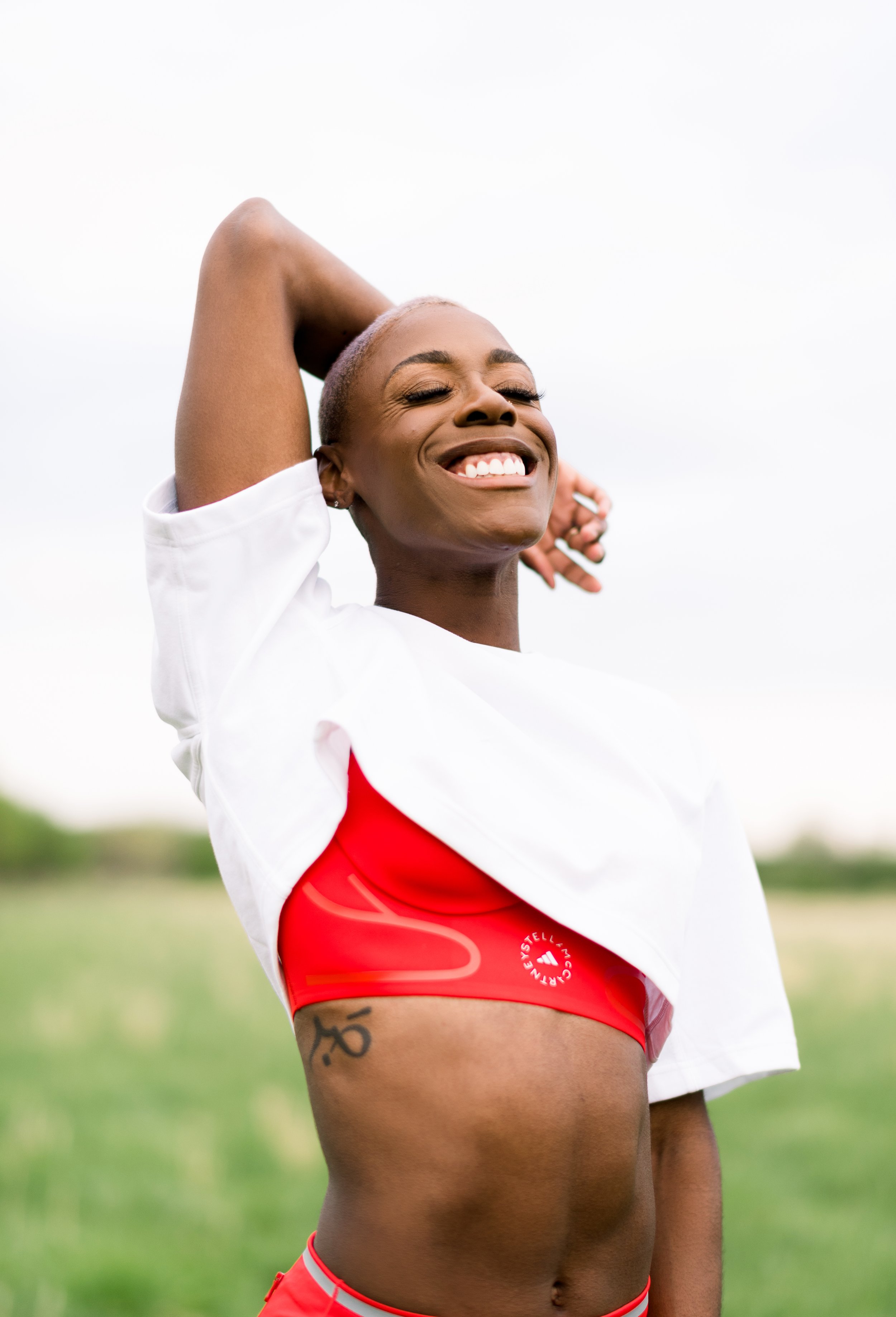 A smiling woman with short blonde hair wearing a white t-shirt and red sportswear outdoors