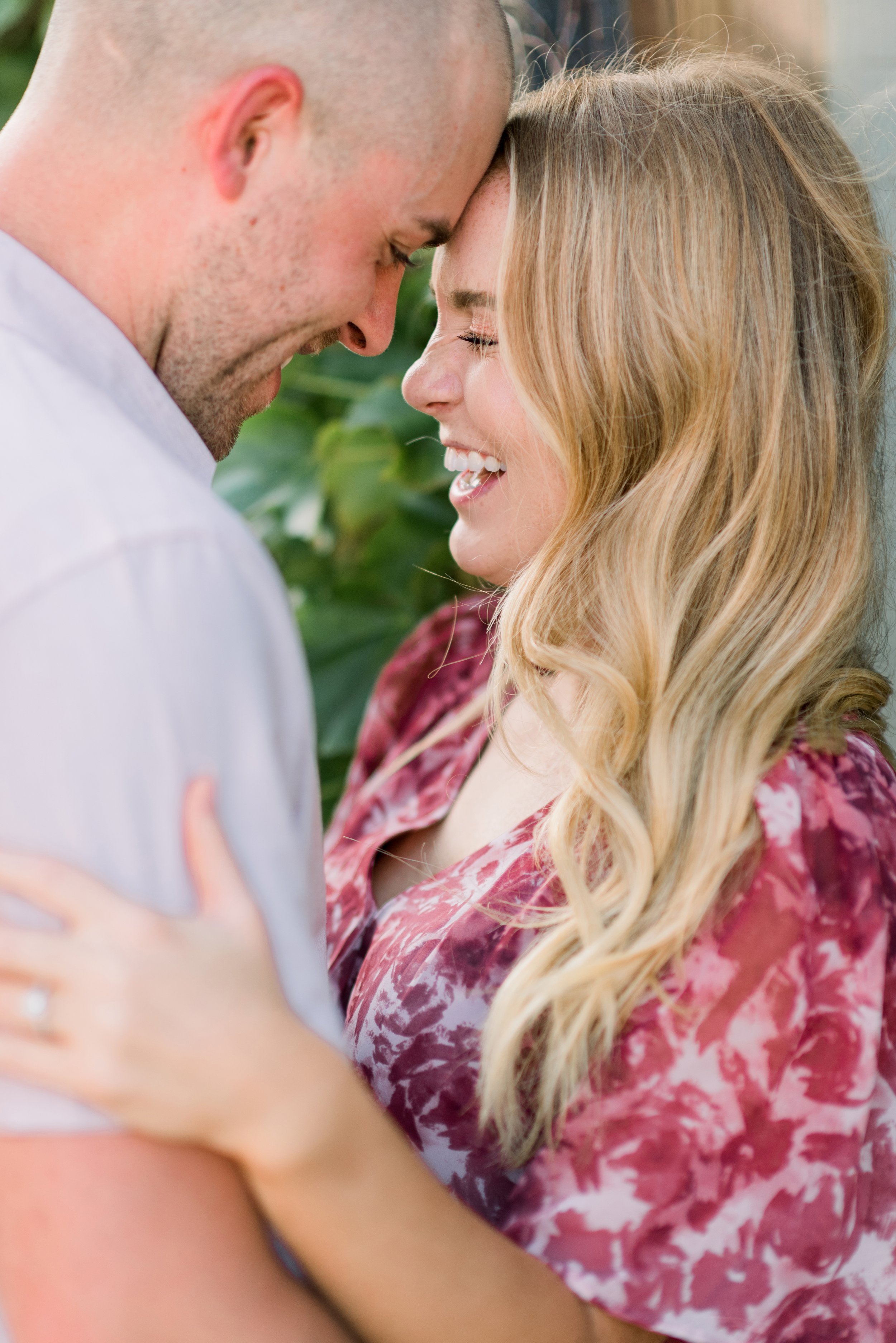 A smiling couple with their foreheads touching, embracing outdoors with a blurred green background.