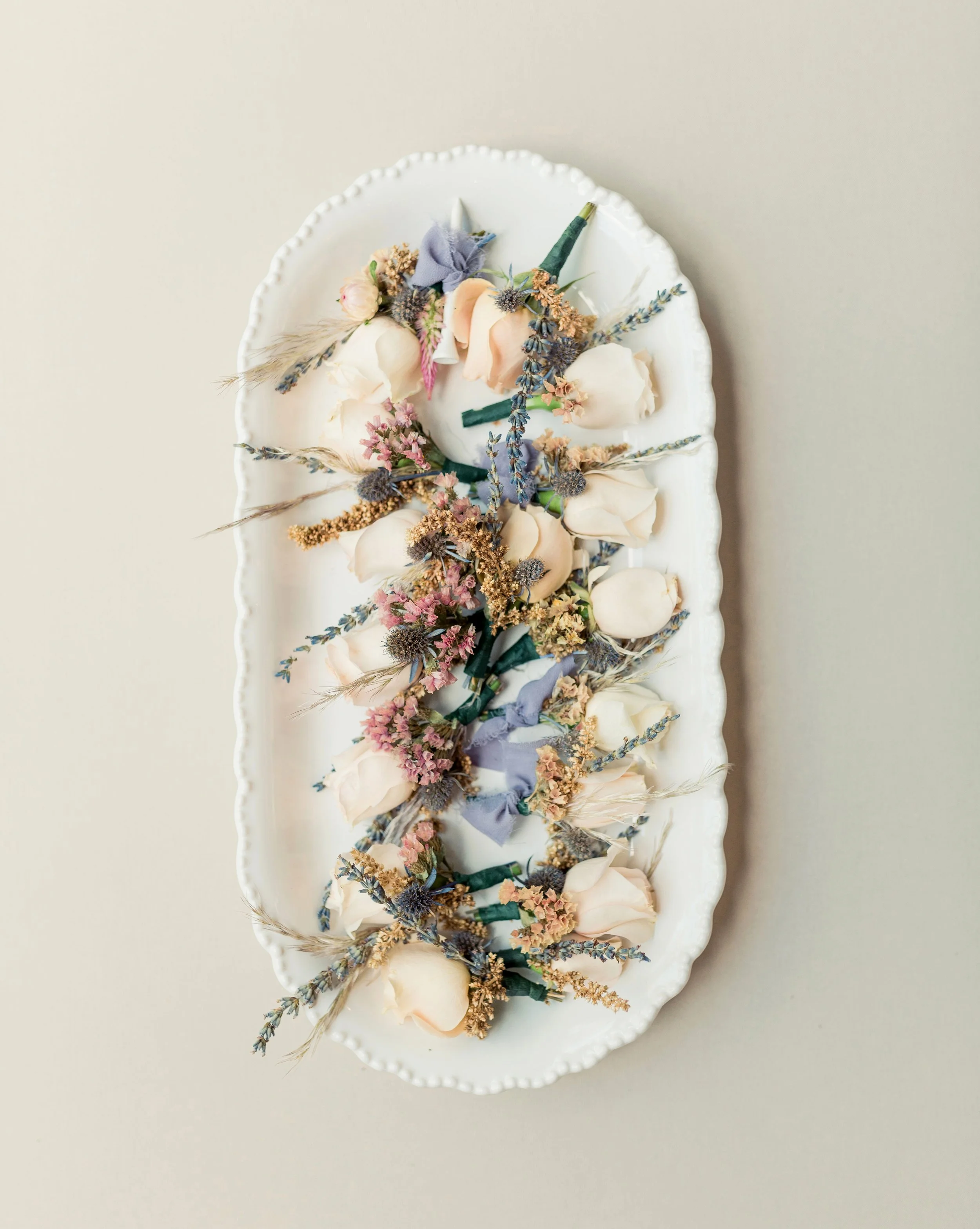 A white oval ceramic plate holding a floral arrangement of dried and preserved flowers with a soft background.