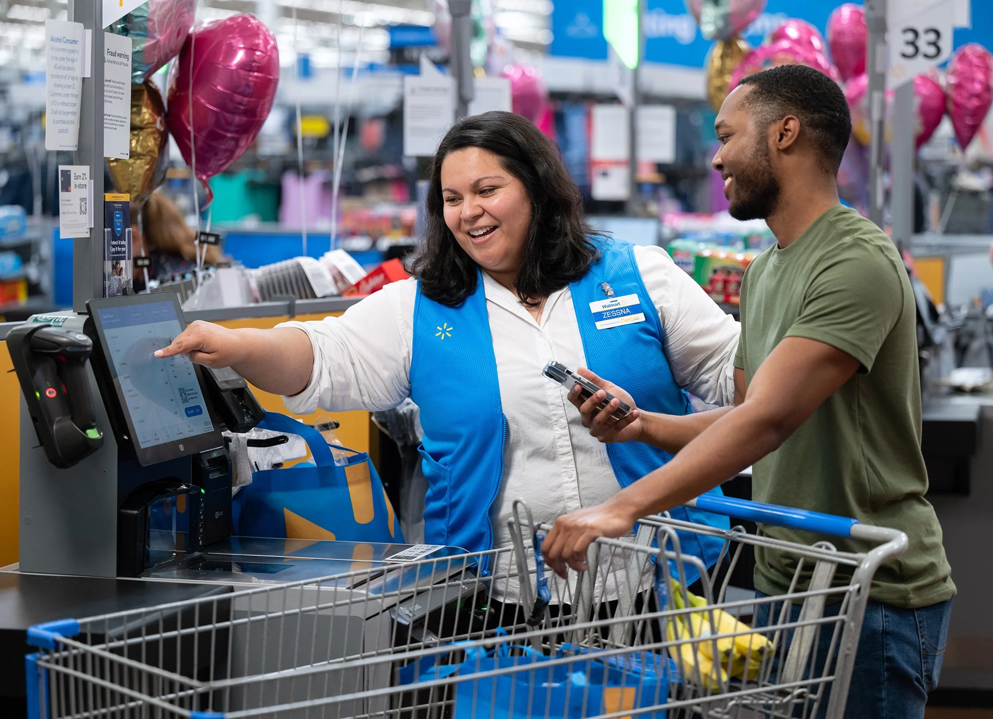 A Walmart cashier smiling and assisting a customer at the checkout in a grocery store.