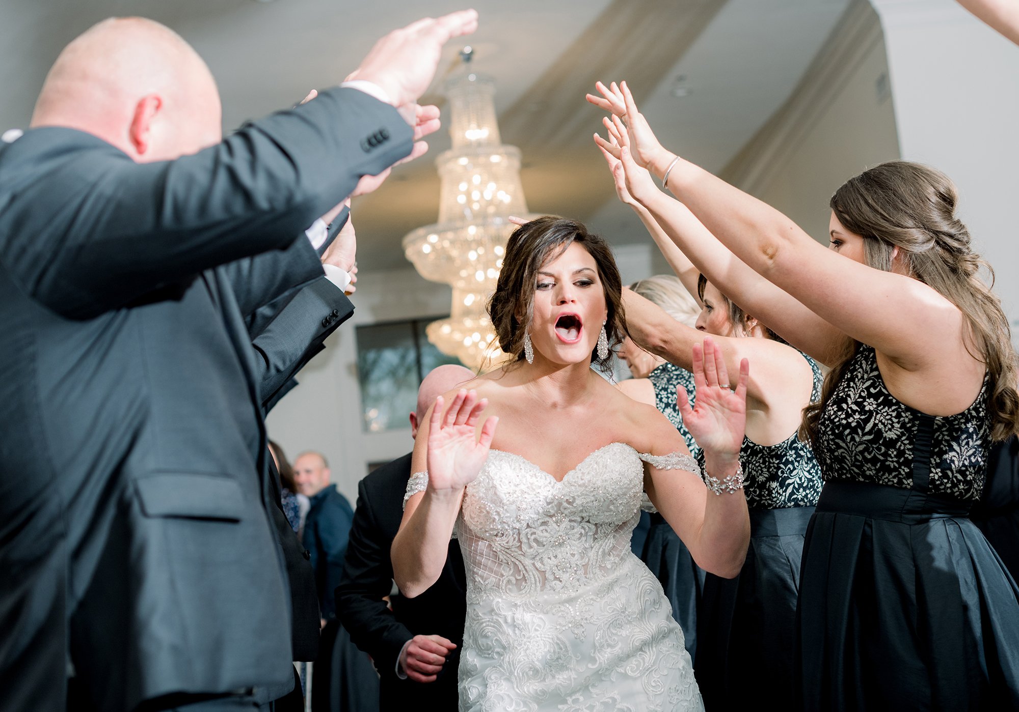 Bride dancing with guests at her wedding reception, surrounded by people raising their hands and enjoying the celebration.