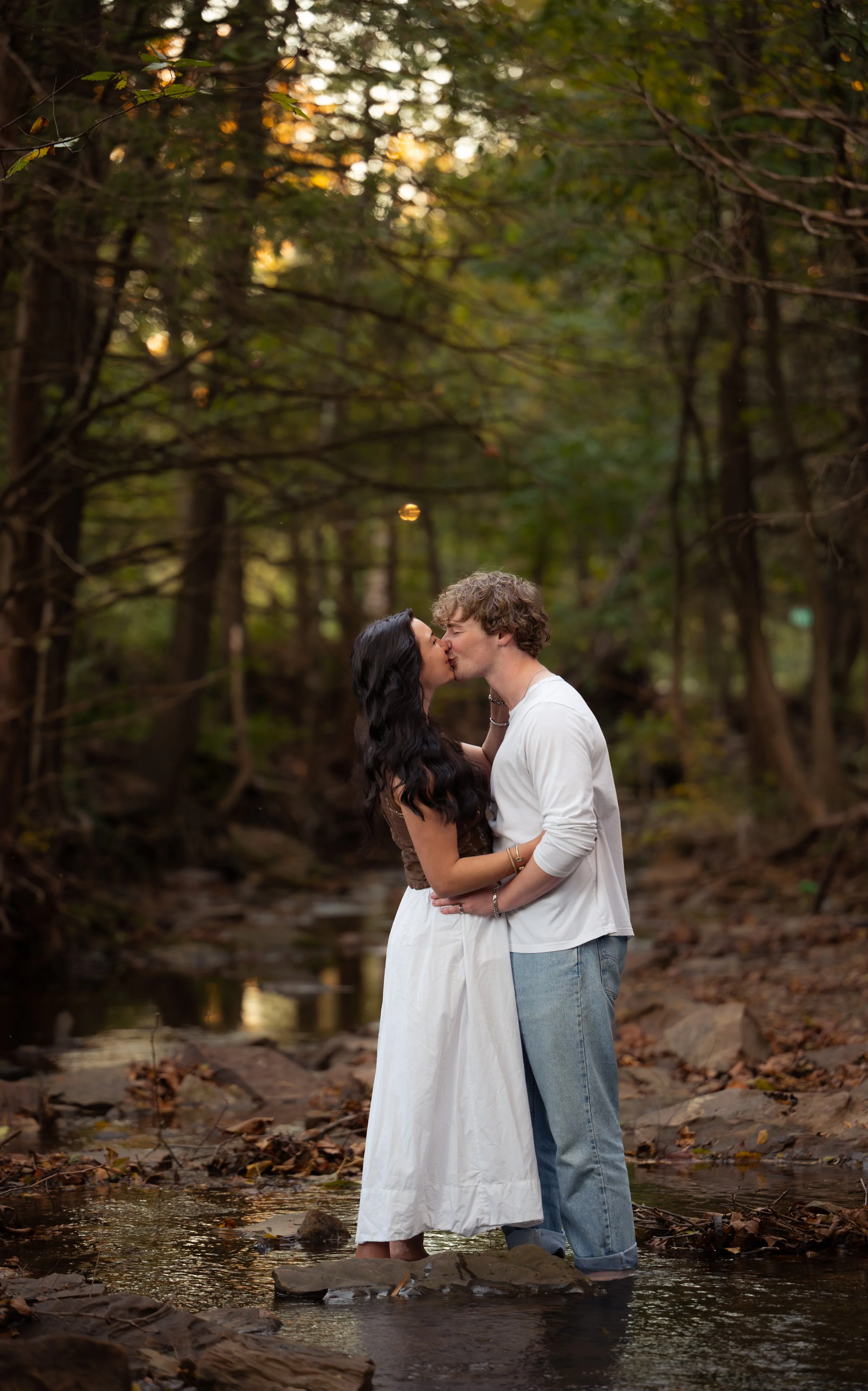 A couple sharing a kiss in a creek surrounded by trees