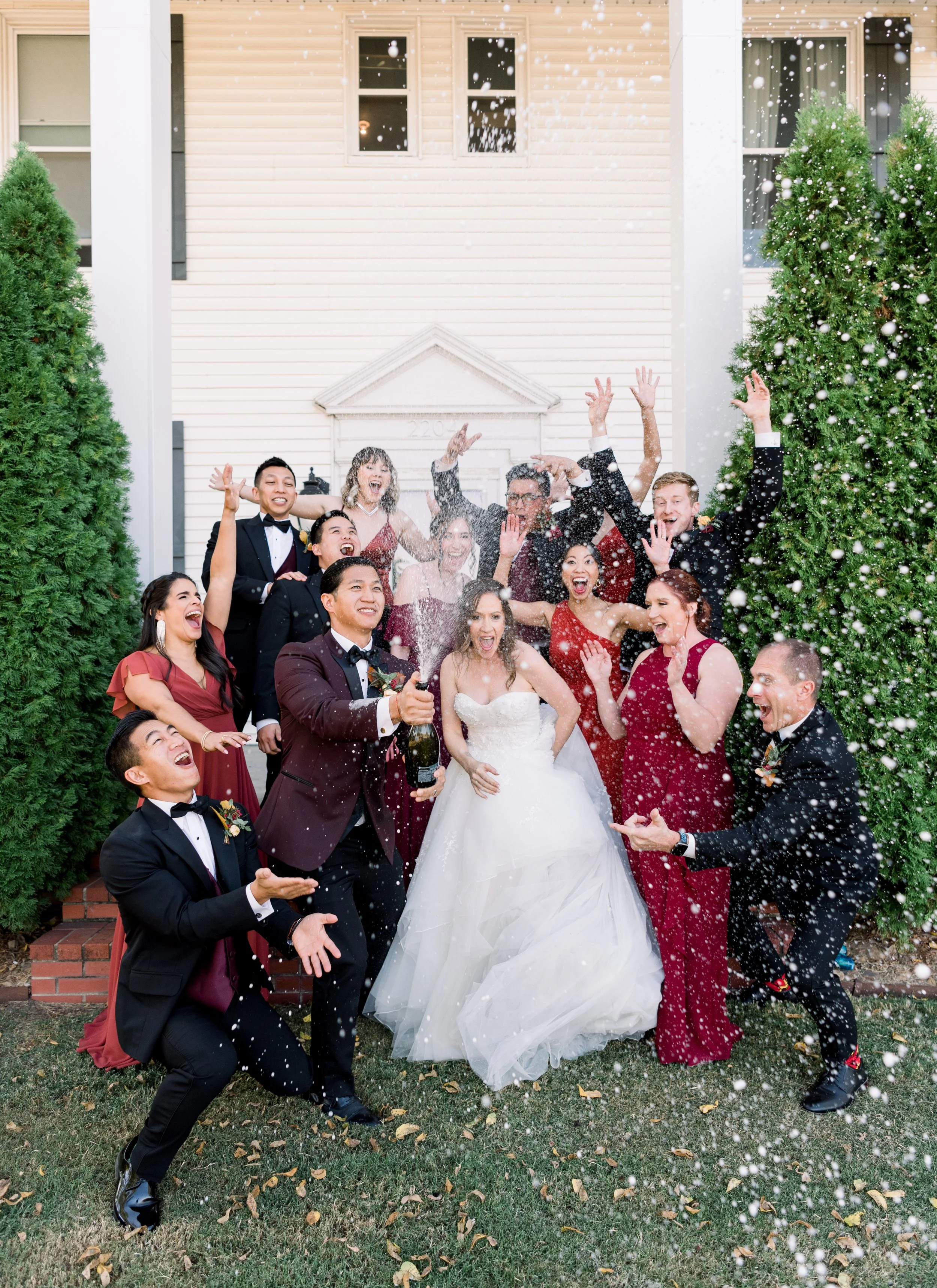 A group of people celebrating at a wedding outside a house, with confetti in the air and everyone smiling and enjoying the moment.