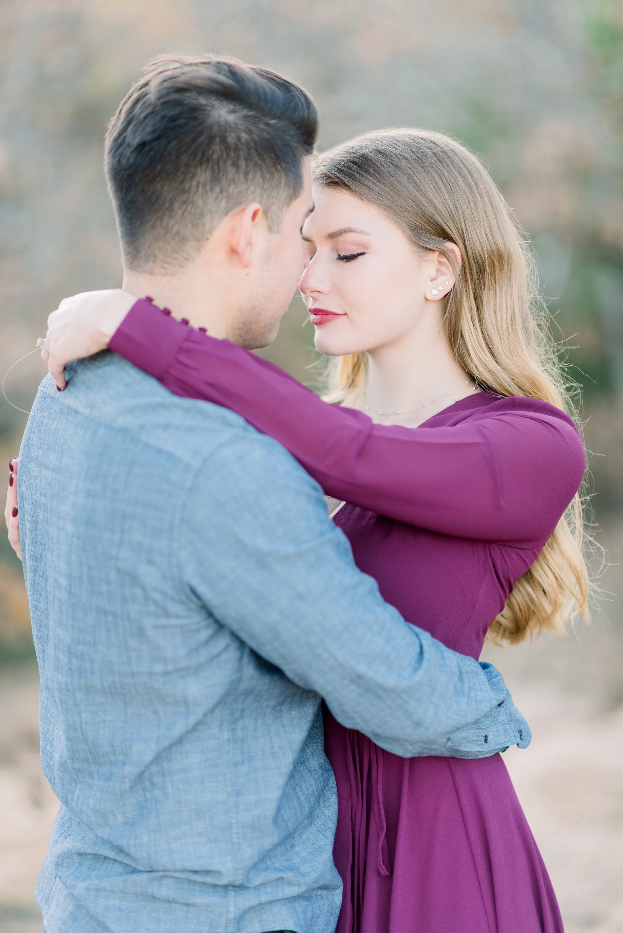 A young couple embraces outdoors with their faces close together, eyes closed, in a loving pose.