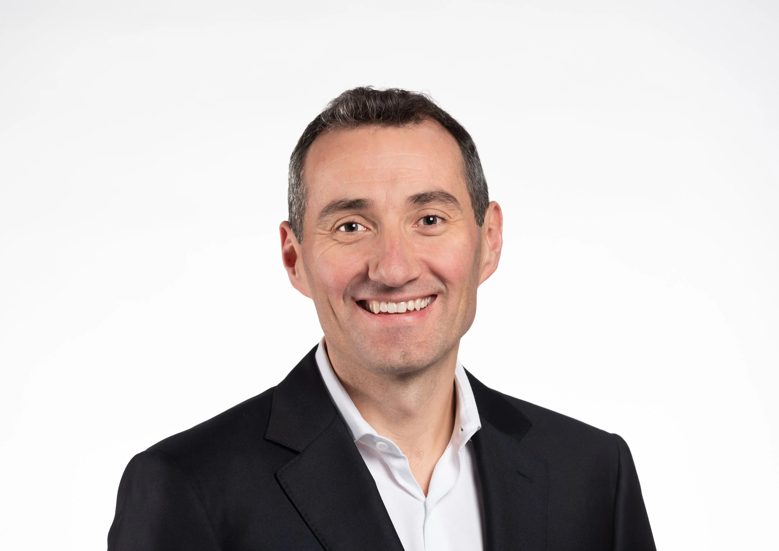 Photograph of a smiling man in a black suit and white shirt, against a plain white background.