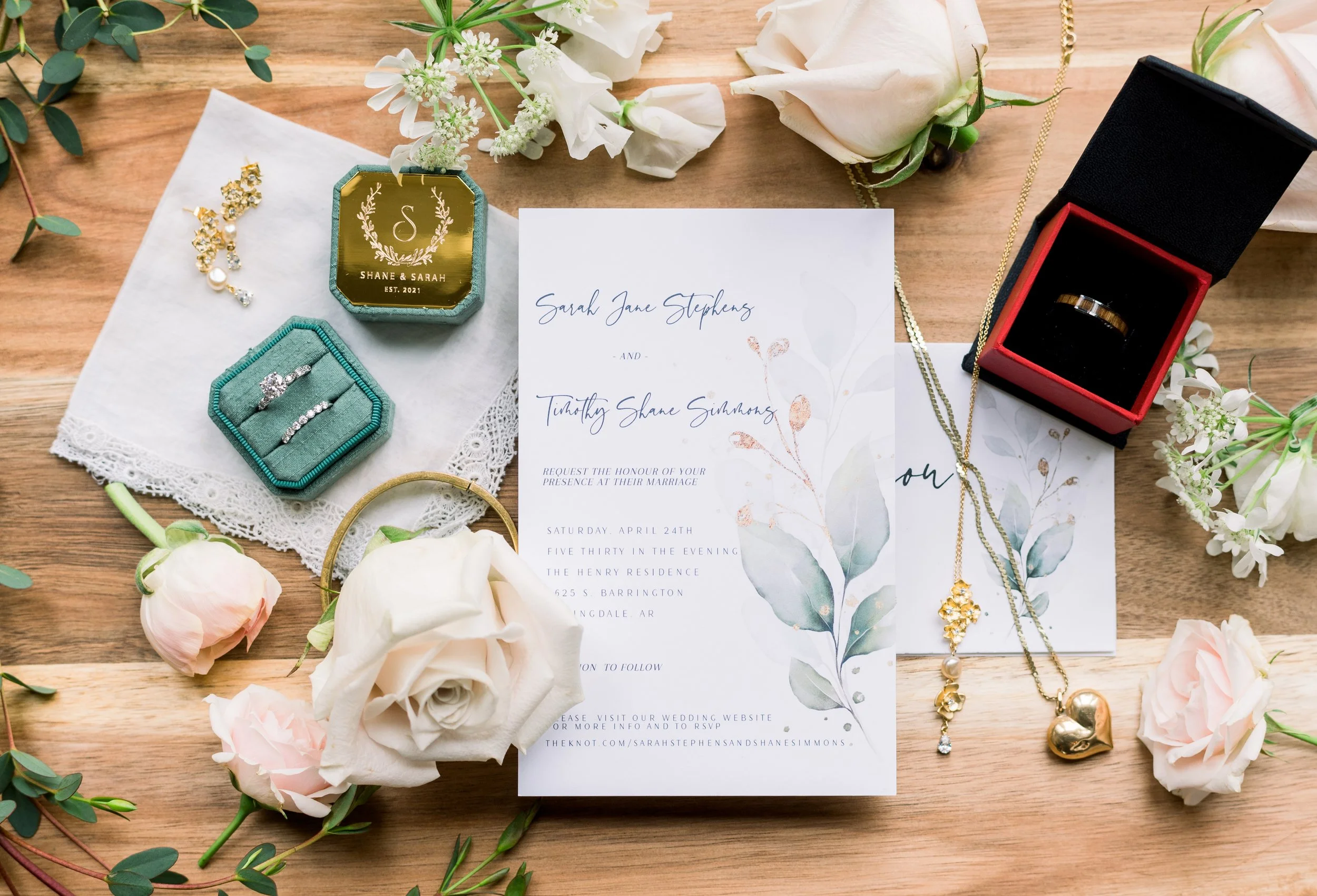 Wedding invitation surrounded by jewelry, flowers, and wedding accessories on a wooden surface.