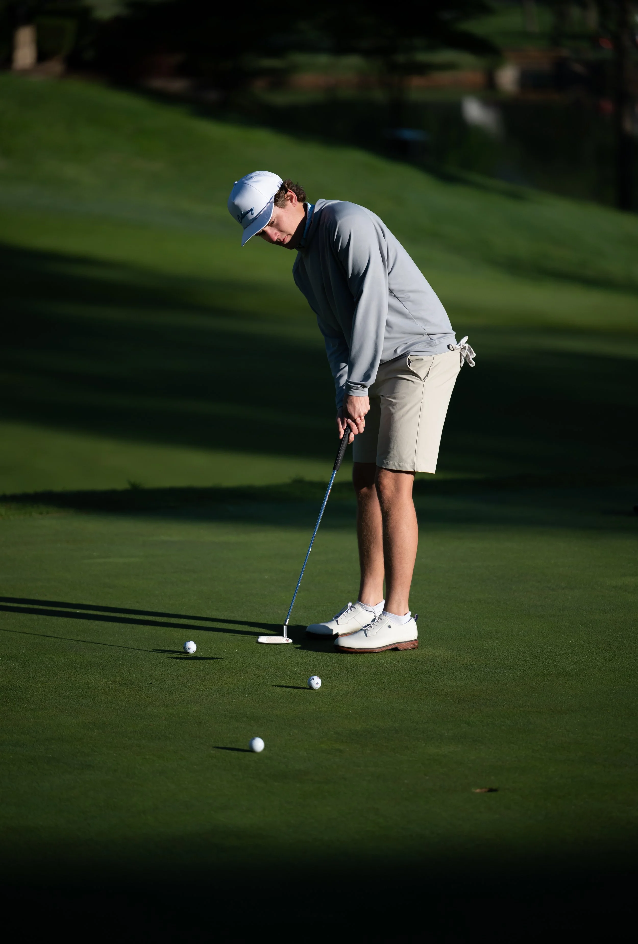 A man playing golf on a green, preparing to putt with several golf balls around him.