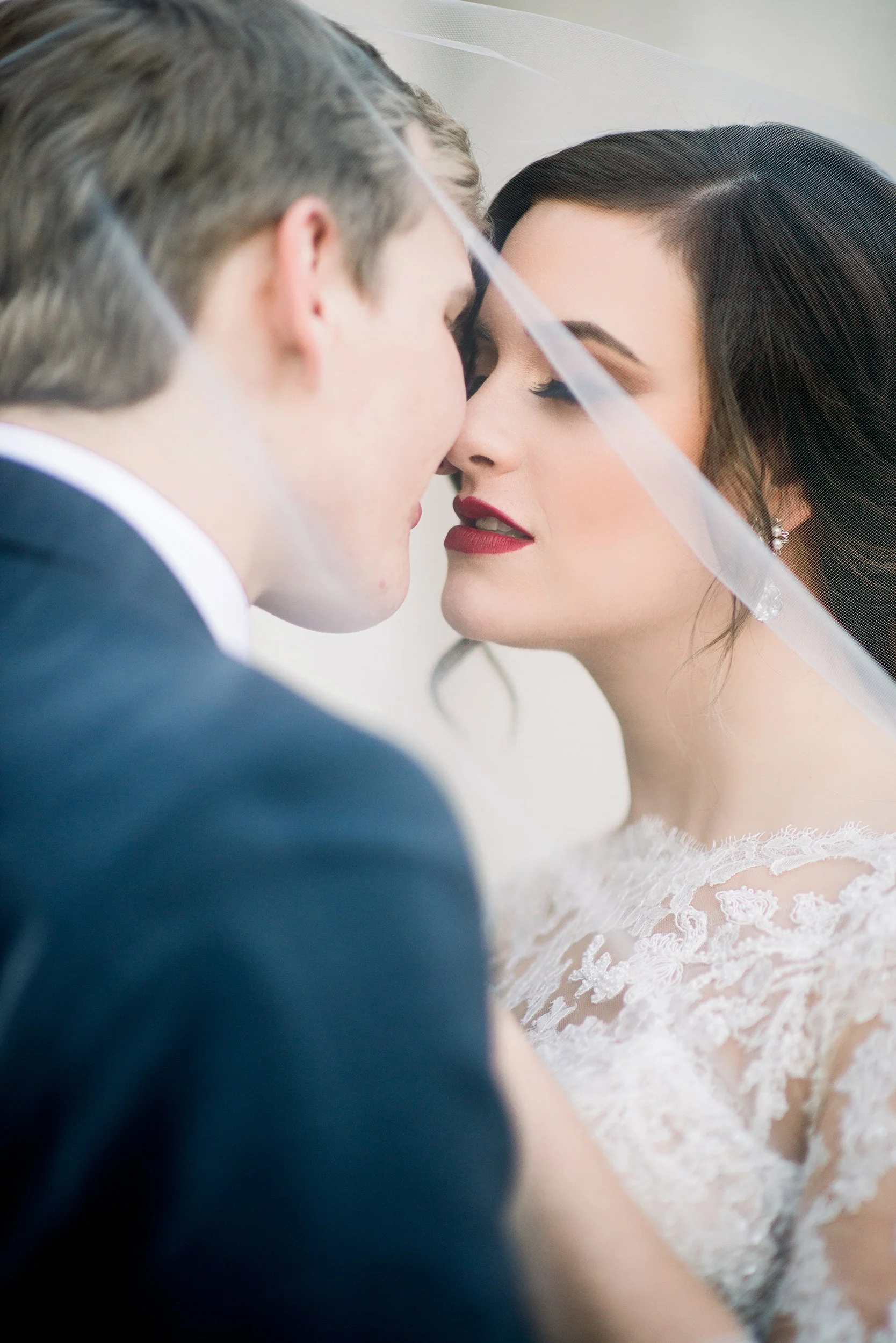 Close-up of a bride and groom with foreheads touching, eyes closed, behind a semi-transparent veil.