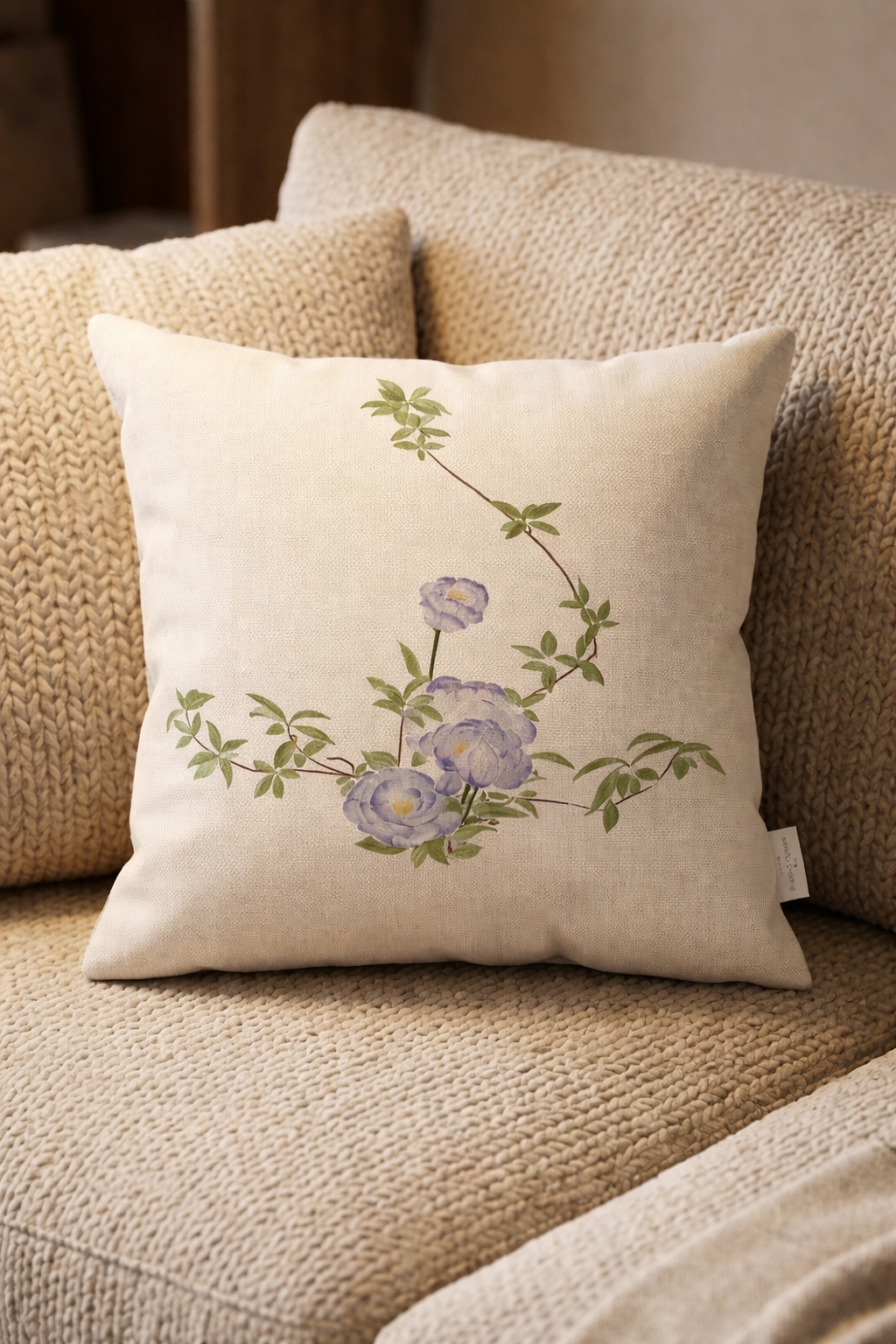 Decorative cushion with purple flowers and green leaves on a beige knitted sofa.