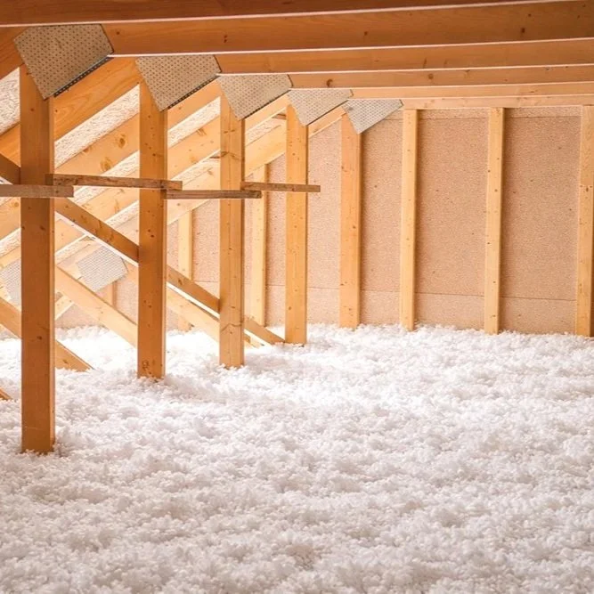 Empty attic with blown-in white fiberglass, exposed wooden framing and sloped ceiling.