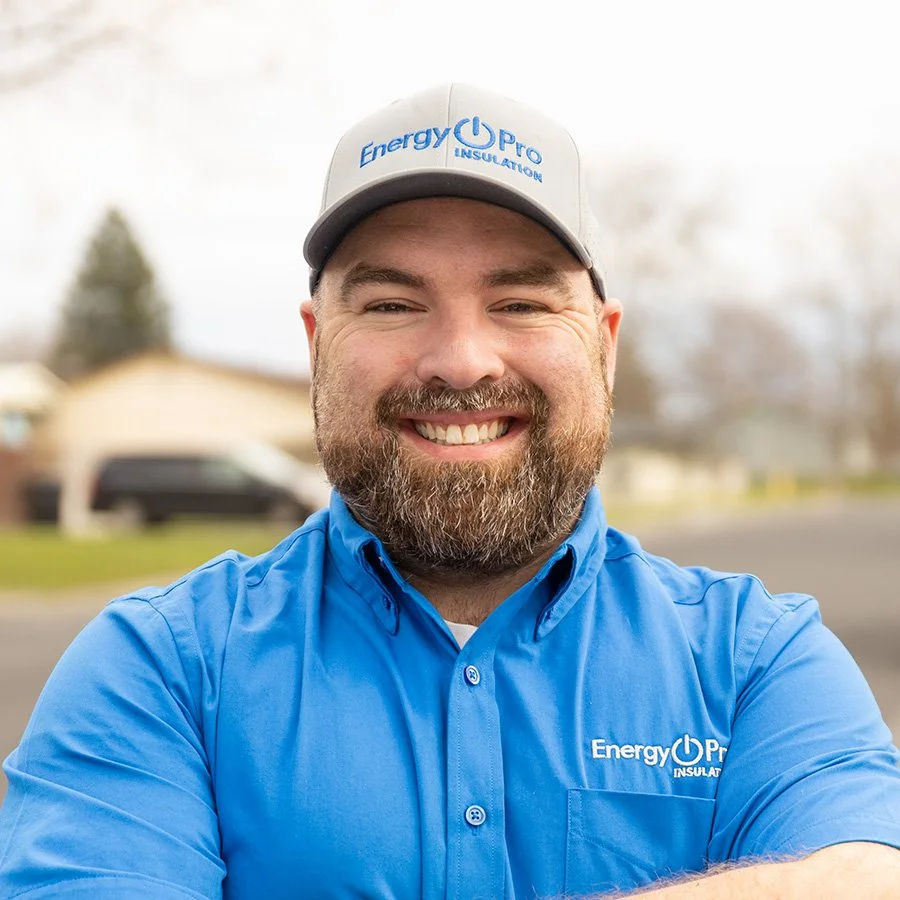 A smiling man wearing a blue shirt and a gray cap with 'Energy Pro Insulation' logo, standing outdoors on a cloudy day.