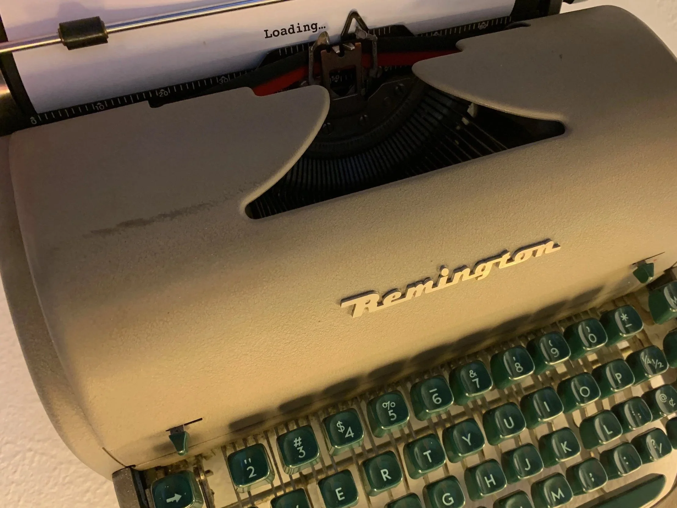 Close-up of a vintage beige Remington typewriter with green keys and a piece of paper loaded, displaying the word 'Loading...' at the top.