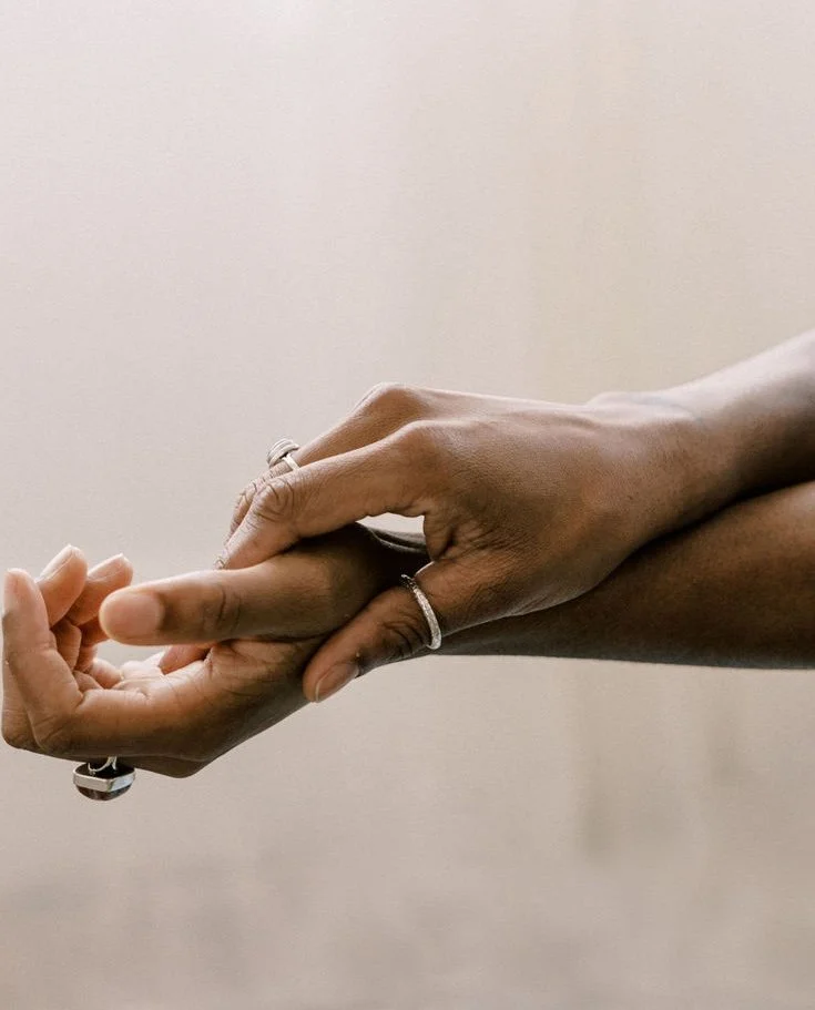 Two hands gently holding each other, with rings on fingers, against a plain background.