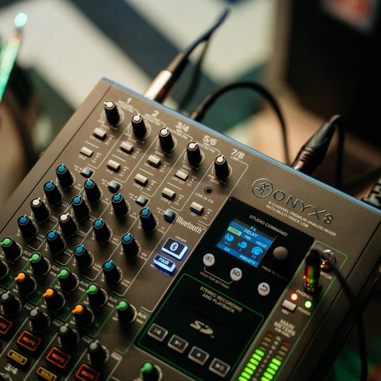 Professional audio mixer with knobs, sliders, and a digital display, connected to several cables.