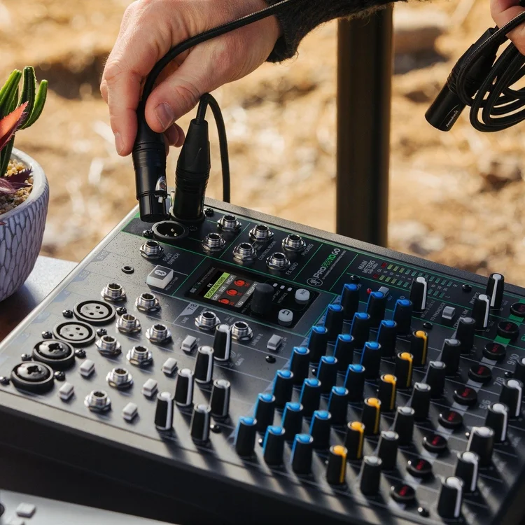 A person adjusting audio equipment on a mixing console outdoors, with a potted plant nearby.