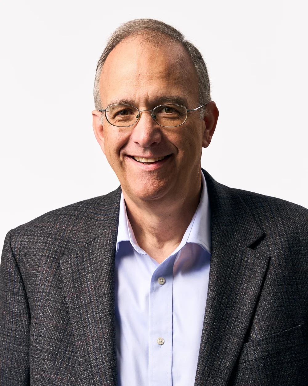 Portrait of a smiling middle-aged man with glasses, wearing a dark blazer and a light blue shirt, against a plain white background.