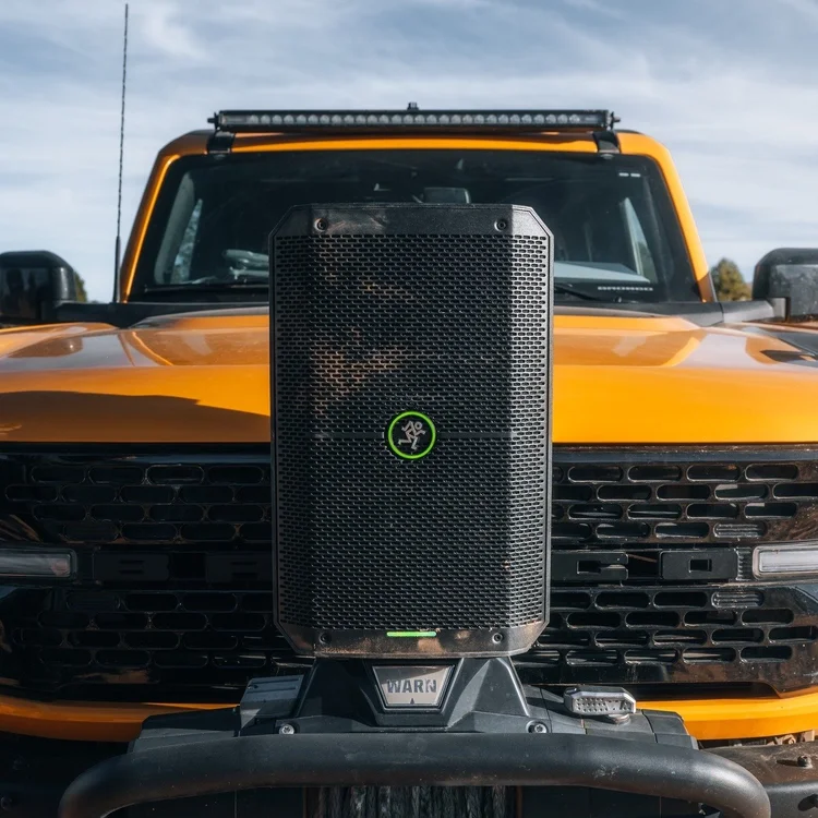 Close-up of a yellow off-road vehicle, possibly a Jeep or truck, with a large black speaker mounted on the front grille.
