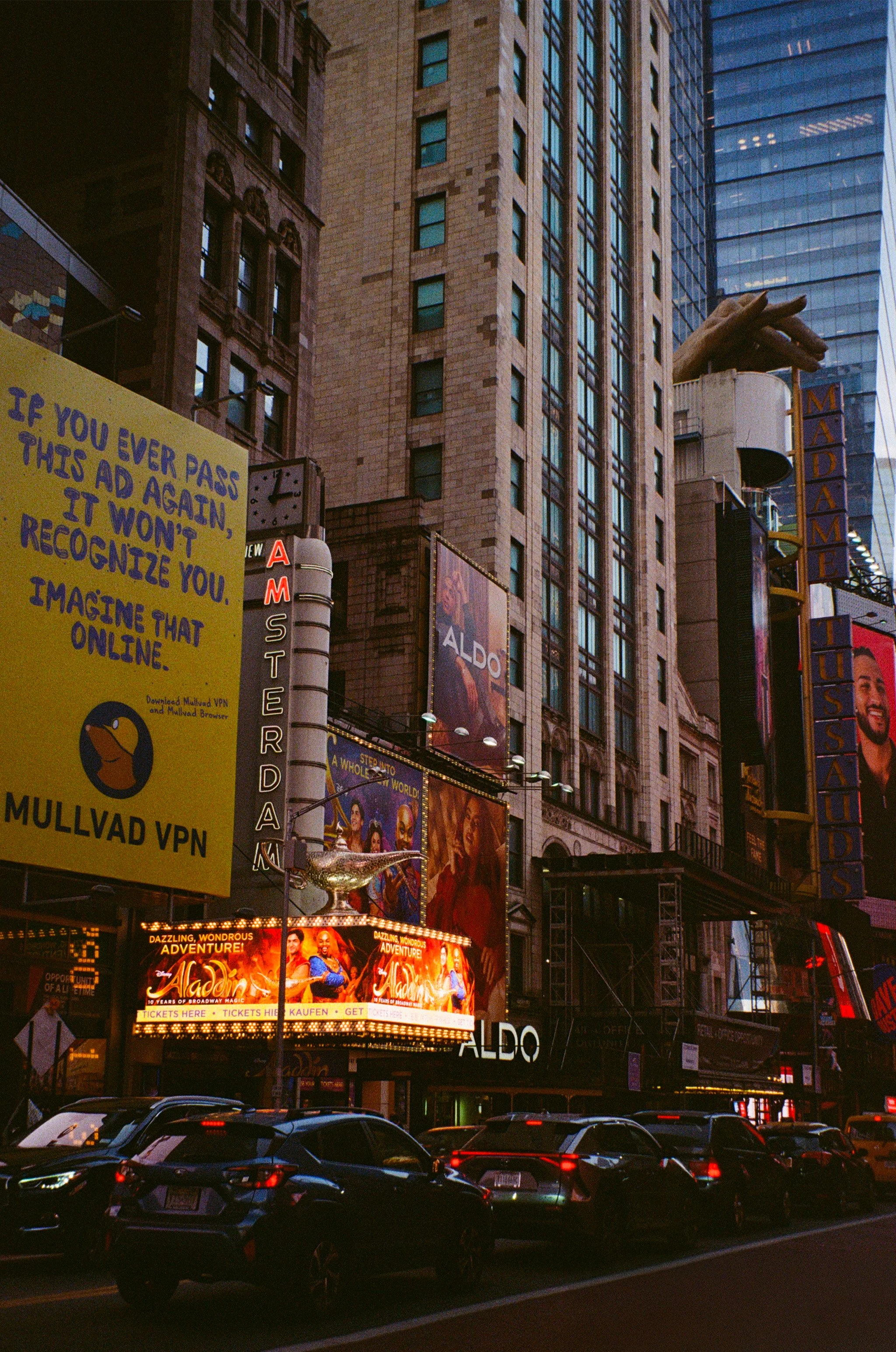 Paysage urbain avec des gratte-ciel, panneaux publicitaires lumineux, voitures et rickshaws dans la rue.