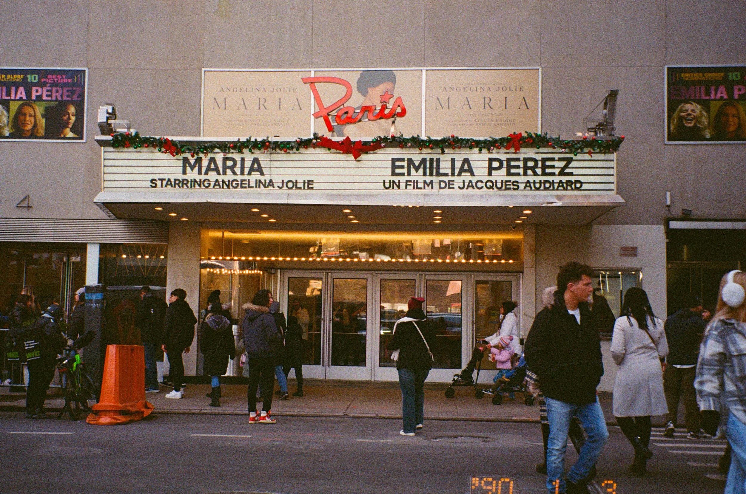 Affiche théâtre pour la pièce "Maria" avec Angelina Jolie et Emilie Perez à Paris. Panneau lumineux, décor de Noël, personnes attendant devant l'entrée, passants.