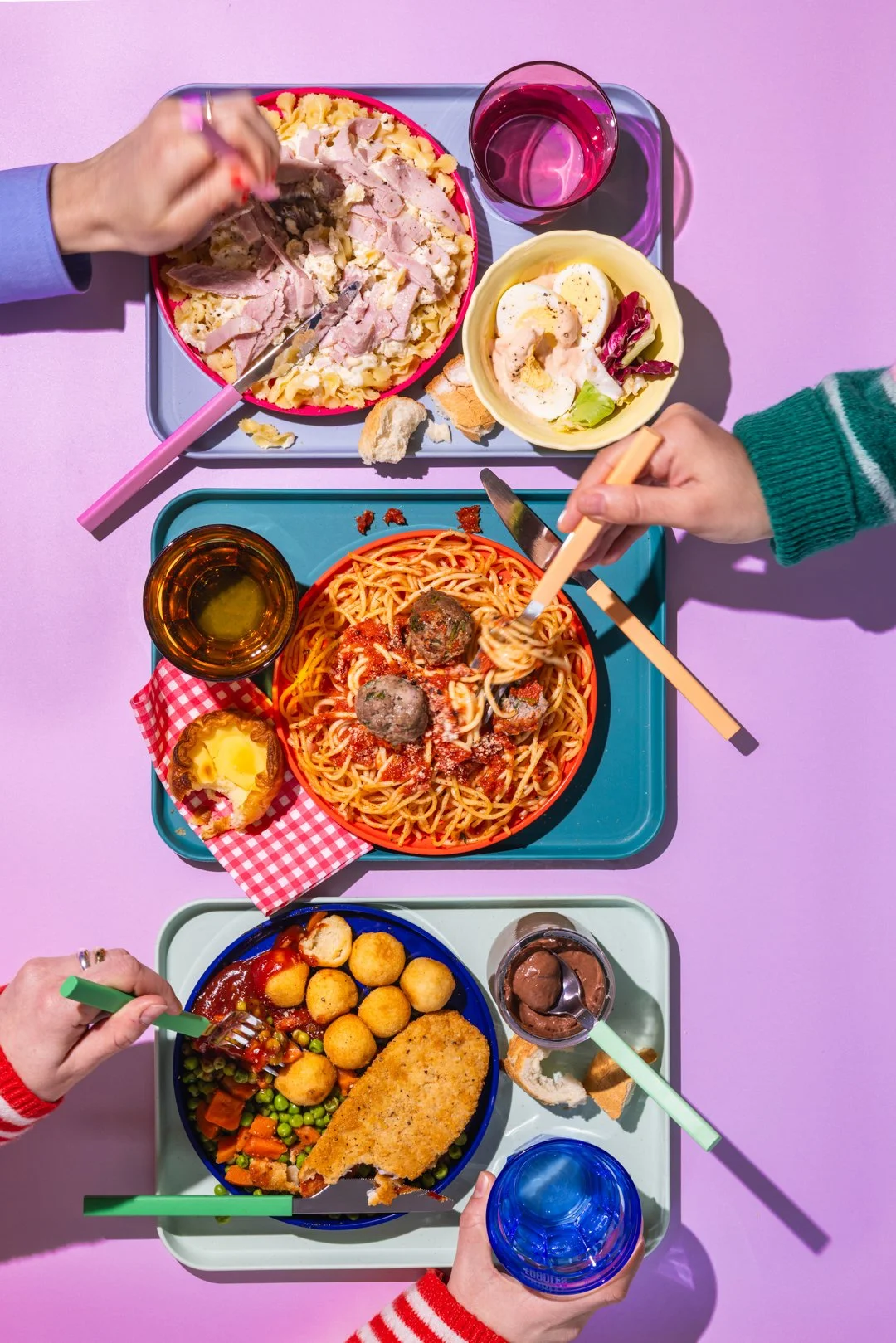 Repas coloré avec pâtes, viande, légumes, dessert et boisson sur une table violette.