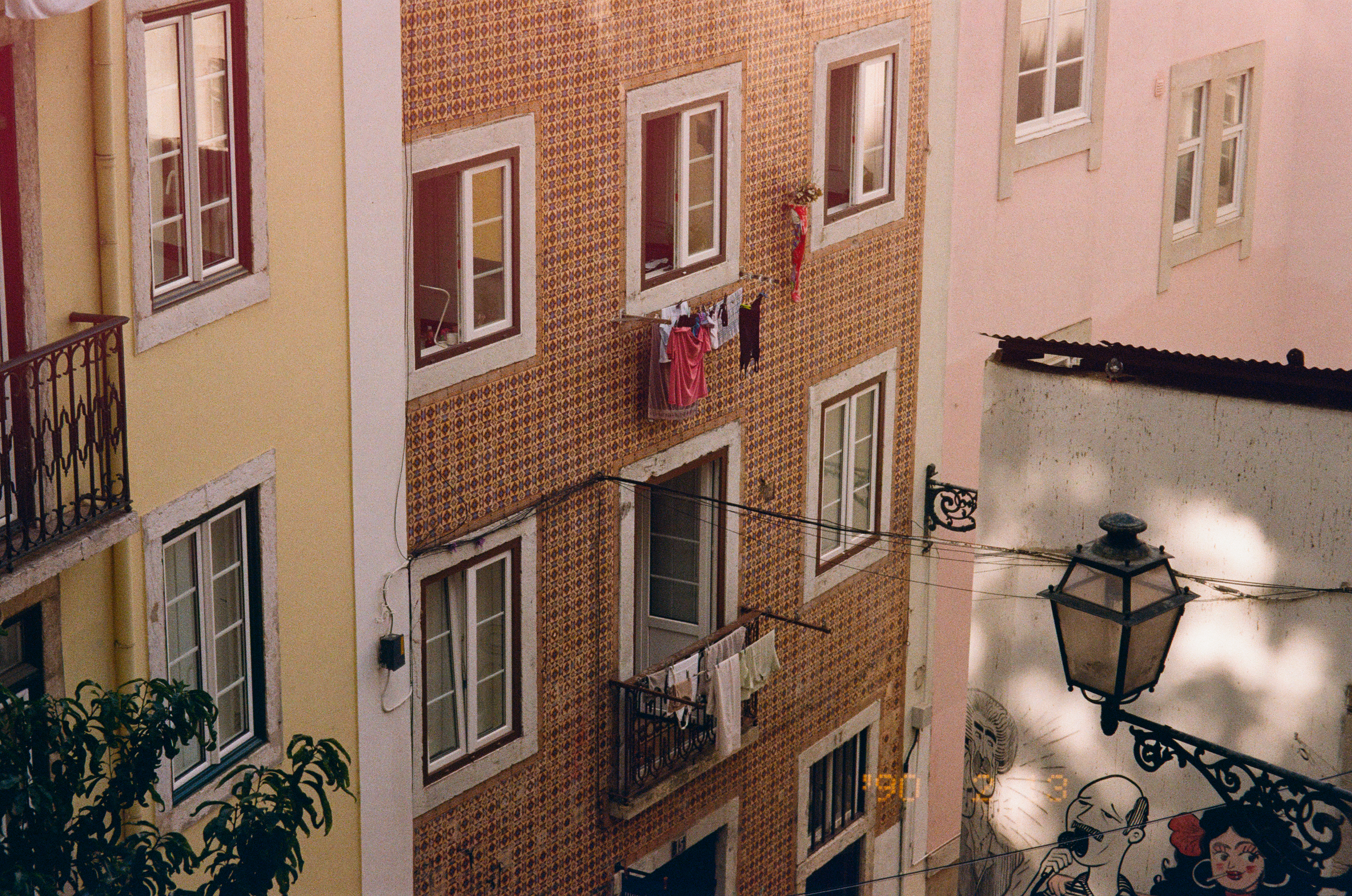 Appartements avec fenêtres ouvertes, des vêtements et linge séchant sur des cordes. Mur en mosaïque colorée sur le bâtiment central, adoucissant l'ambiance urbaine.