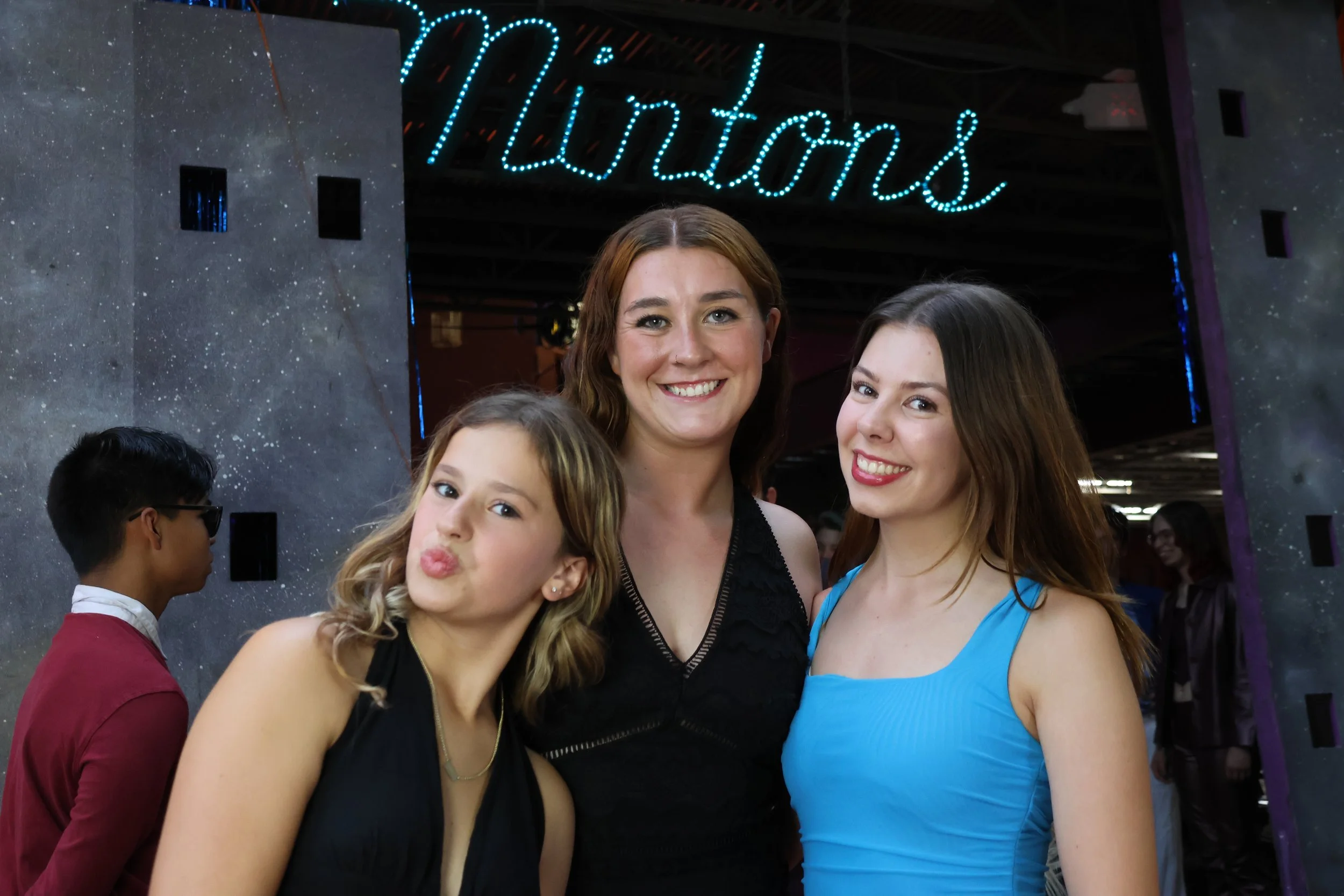 Three young women and a young girl smiling and posing for a photo at a fashion event underneath a neon sign that says 'Foutons'.