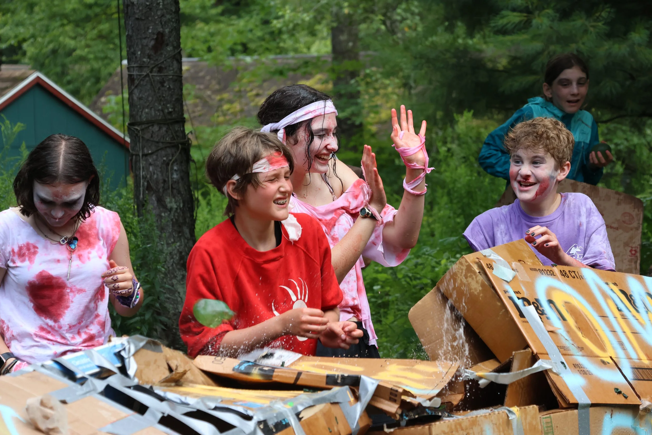Children and a woman celebrating with a box of fireworks or confetti outdoors in a wooded area.