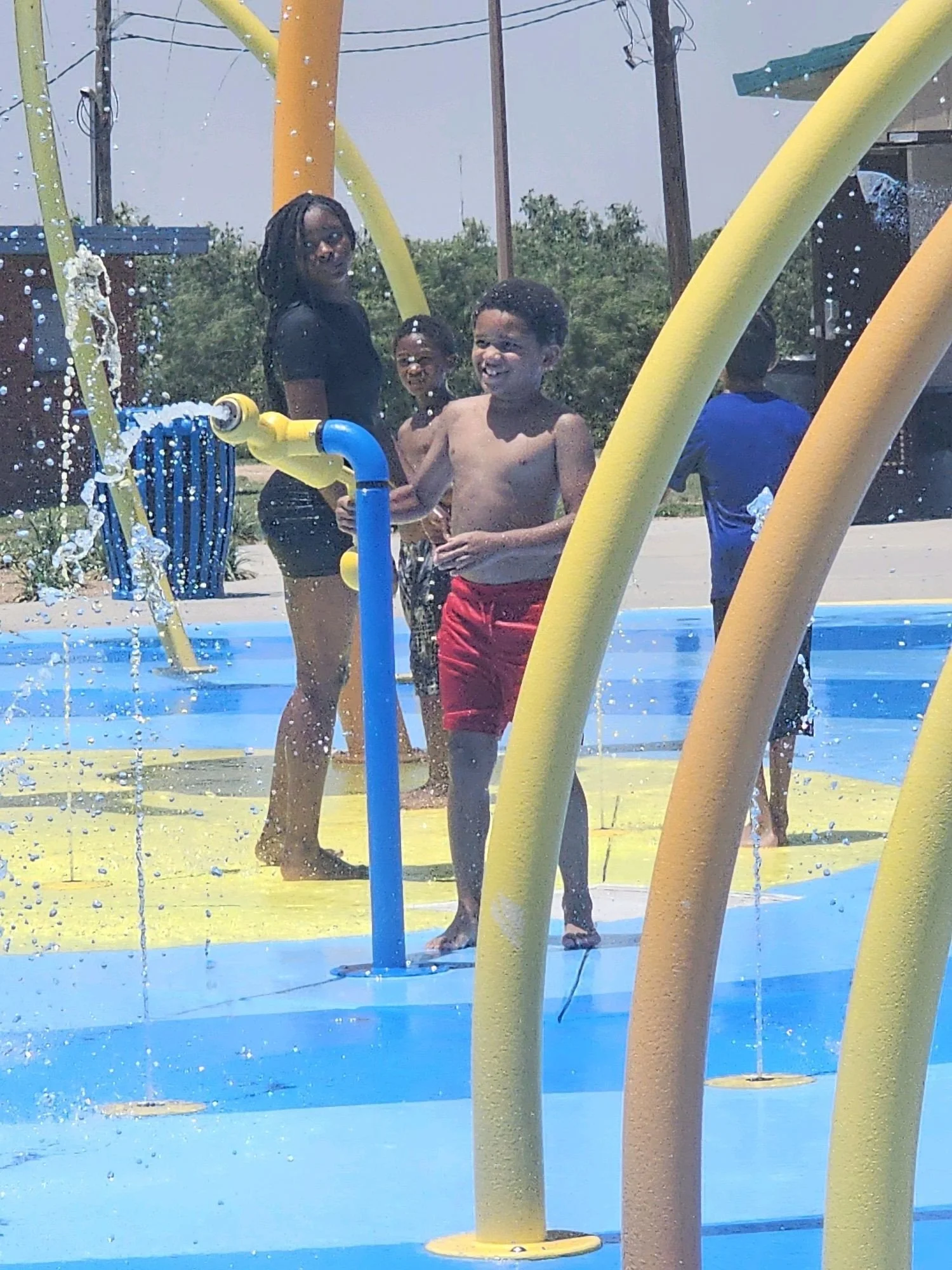 Children playing in a splash pad or water park with yellow and blue structures and water spray.