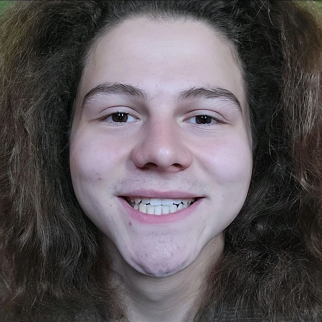 Close-up of a young woman with curly brown hair, smiling, and showing her teeth.