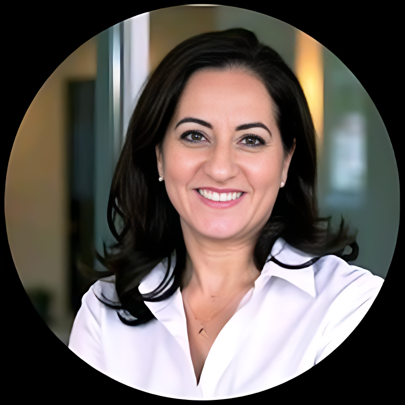 A smiling woman with dark hair, wearing a white blouse, appears to be in a professional setting with blurred background