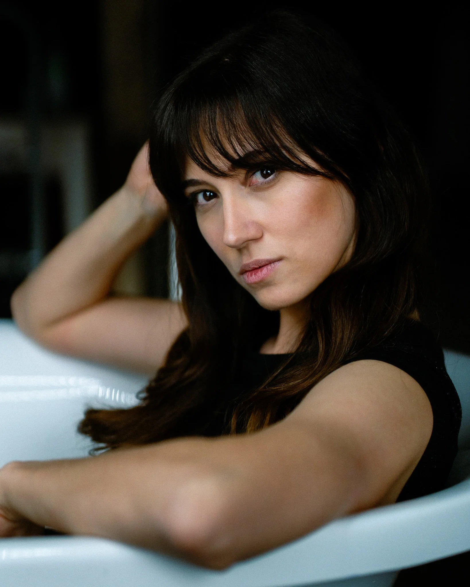 Close-up of a woman with dark brown hair and bangs, looking into the camera, with a blurred background.