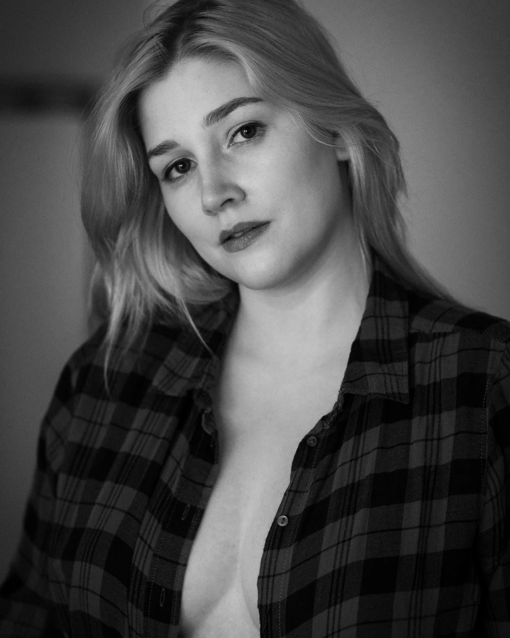 Black and white portrait of a young woman with light-colored hair, wearing a plaid shirt, looking at the camera with a slight smile.