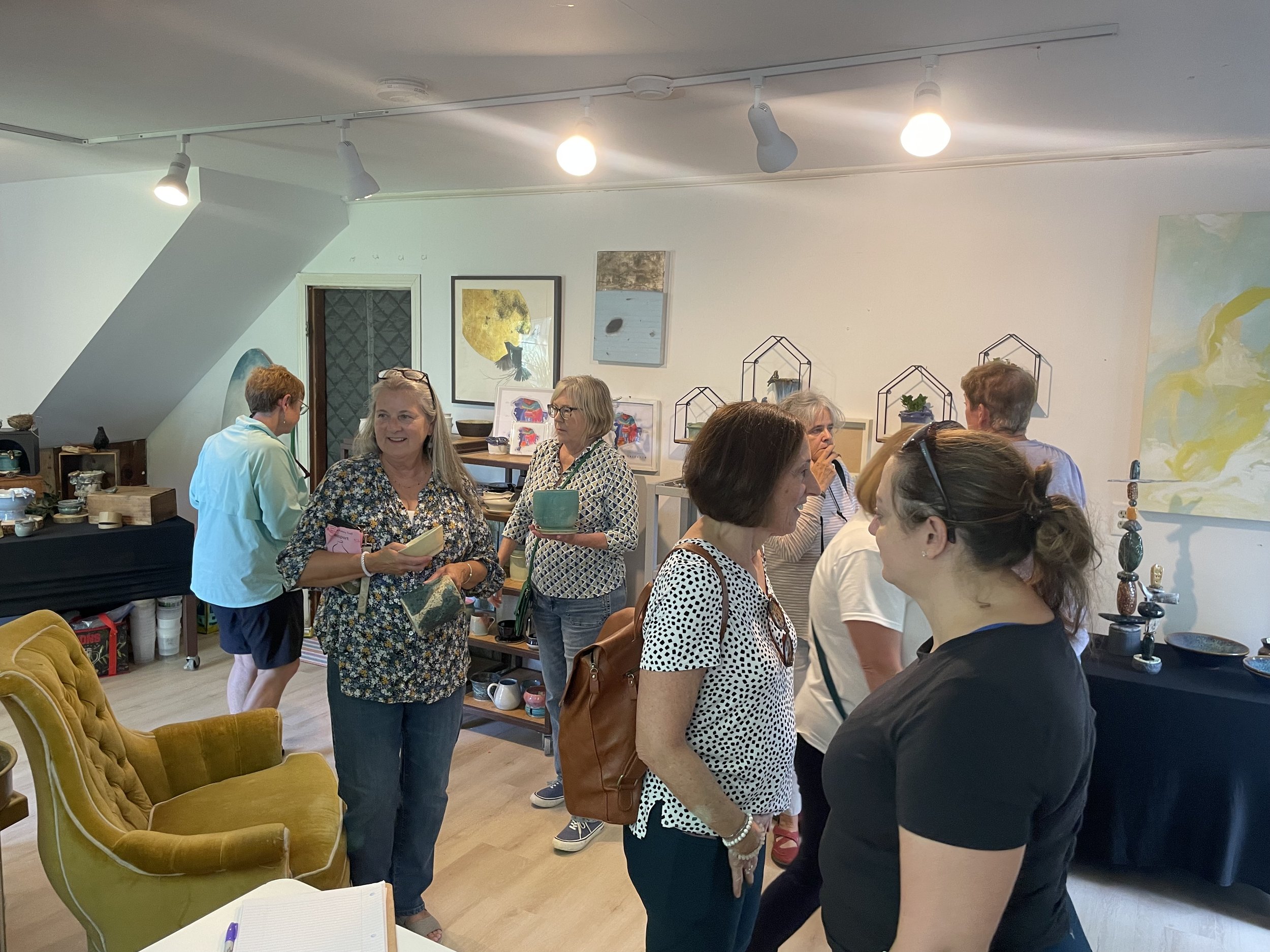 Group of people touring the Perch Pottery studio, with paintings and pottery displayed on walls and shelves.