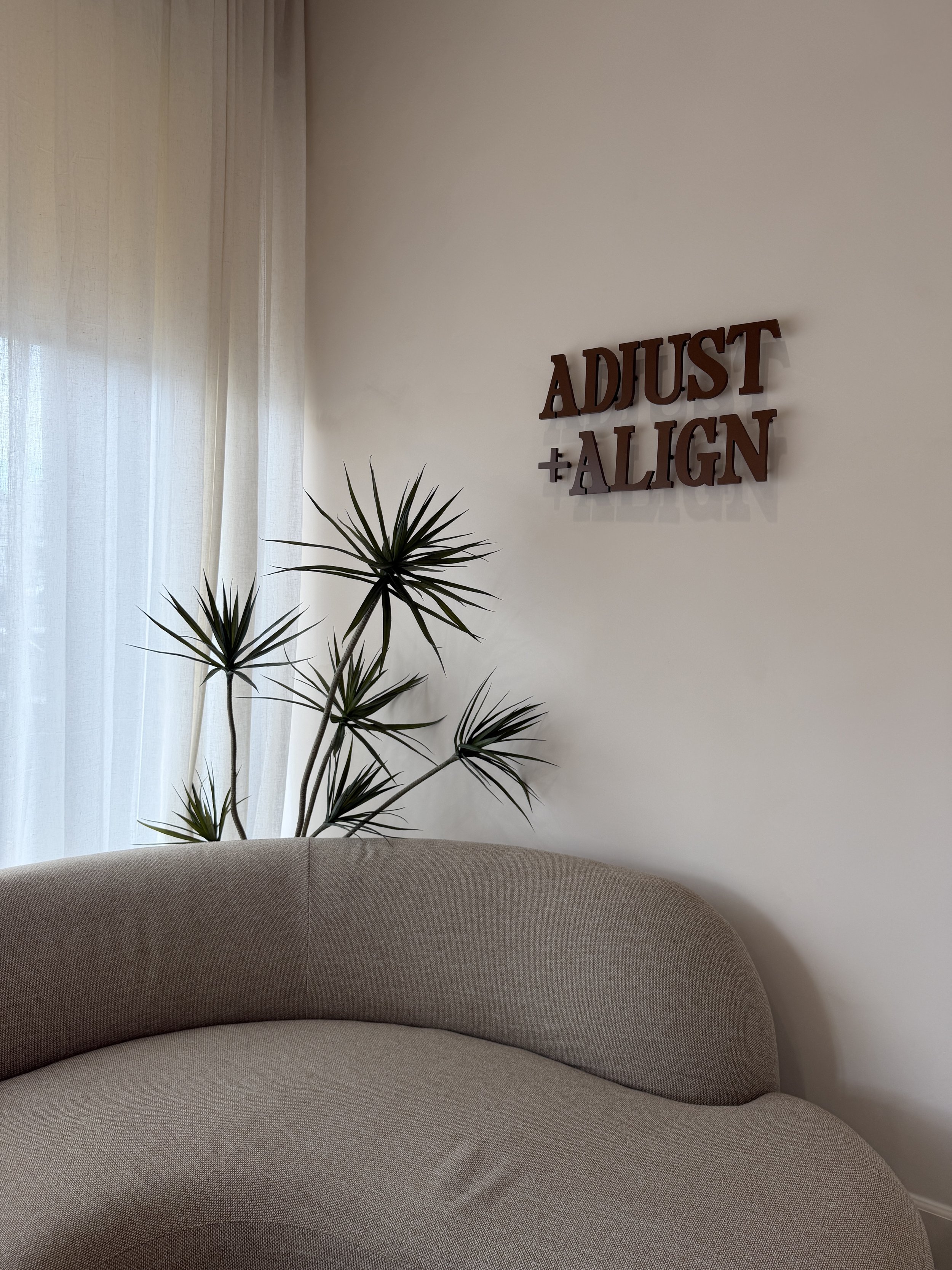 Adjust + Align's waiting area with a curved sofa, plants, and a wall logo sign in the Studio City office