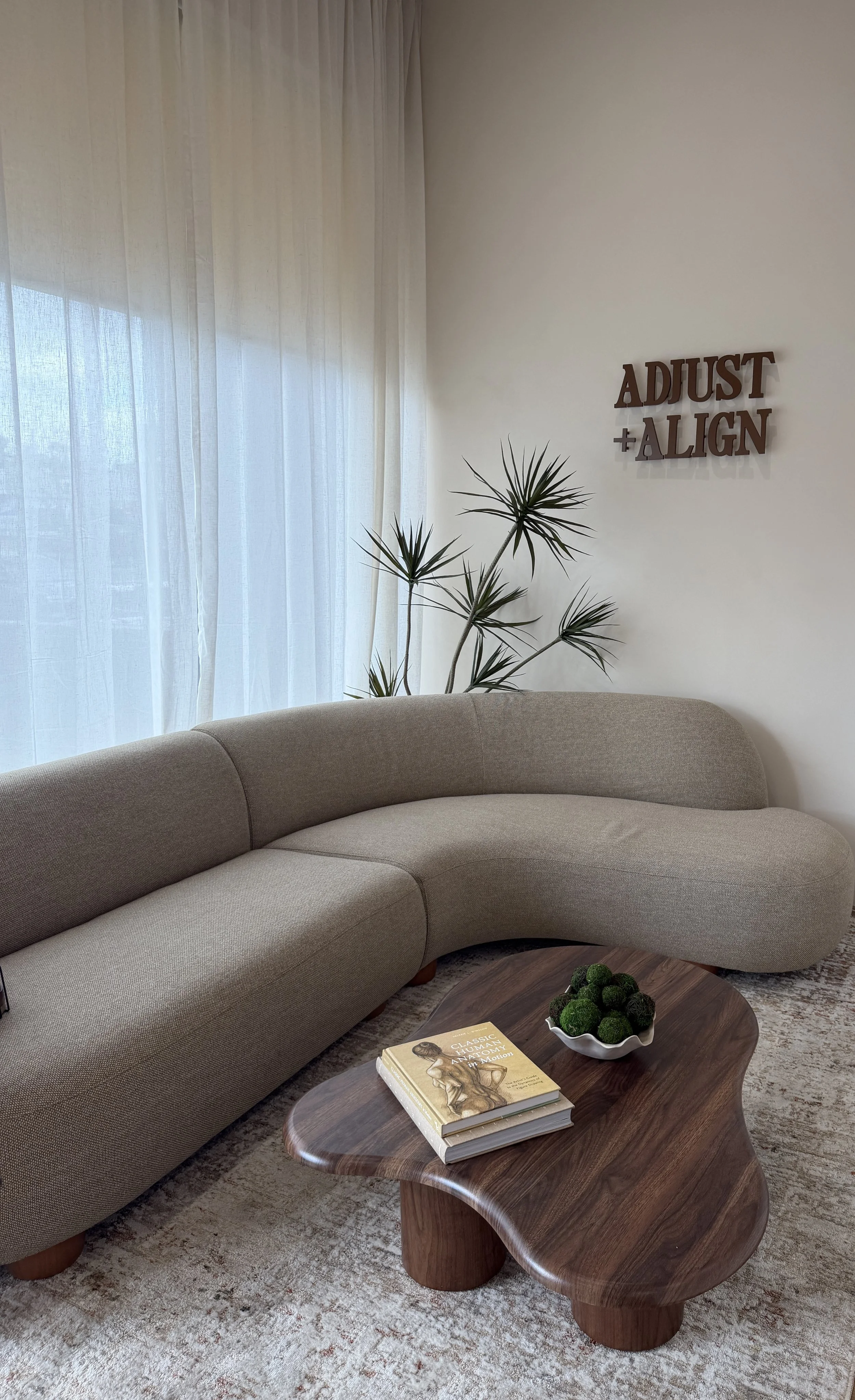 Adjust + Align office interior in Studio City, Los Angeles with a curved sofa, coffee table, and wall logo sign