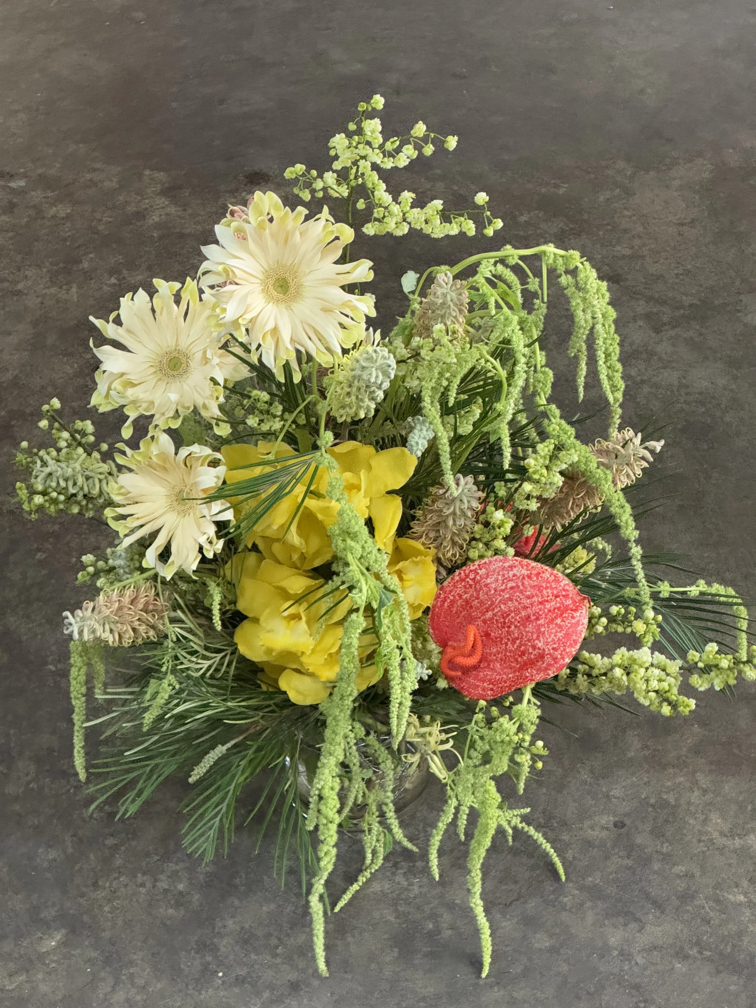 A colorful floral arrangement with cream, yellow, green, pink, and red flowers on a dark textured surface.