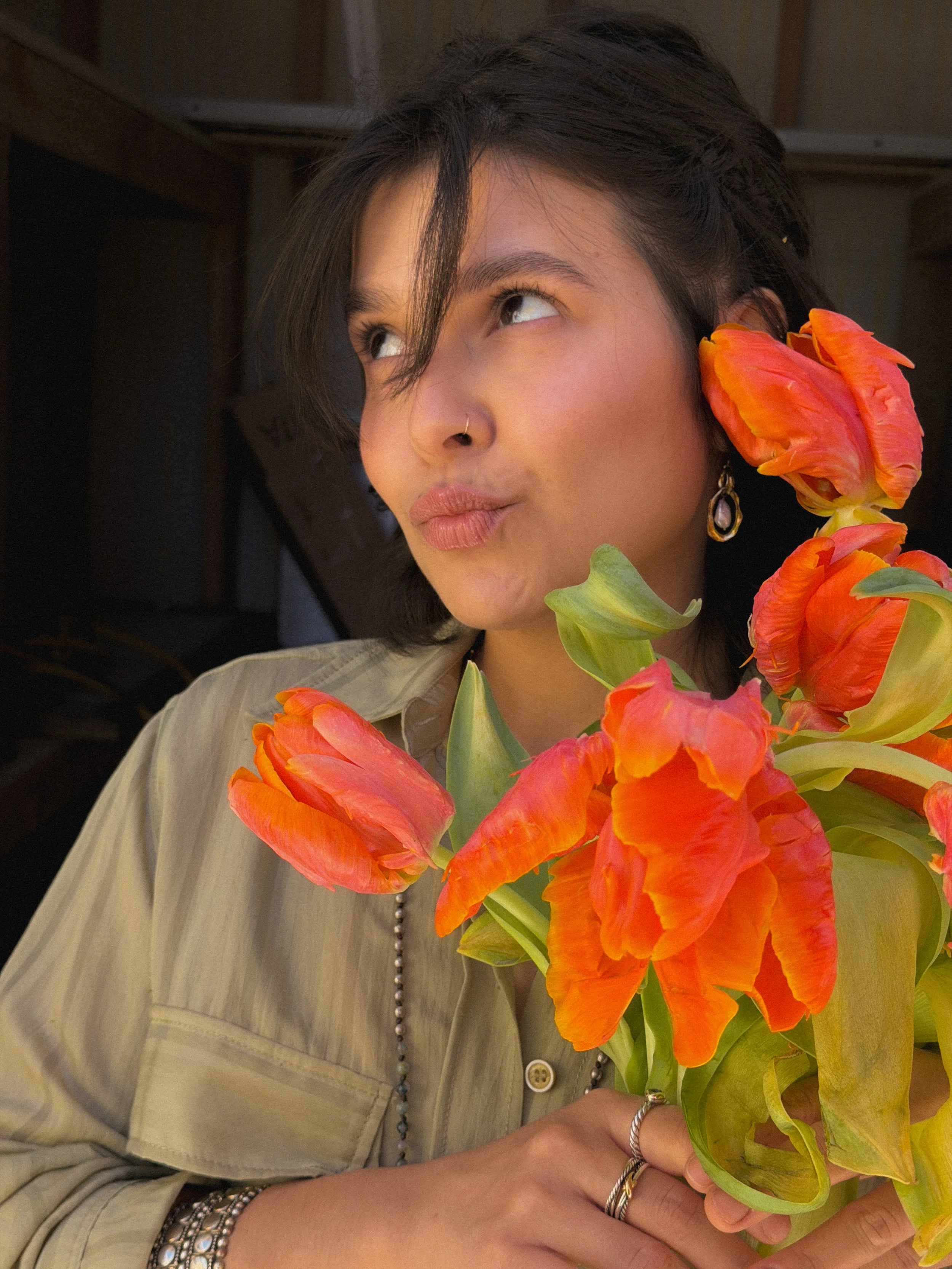 Person with dark hair and jewelry holding a bouquet of colorful orange and pink flowers.