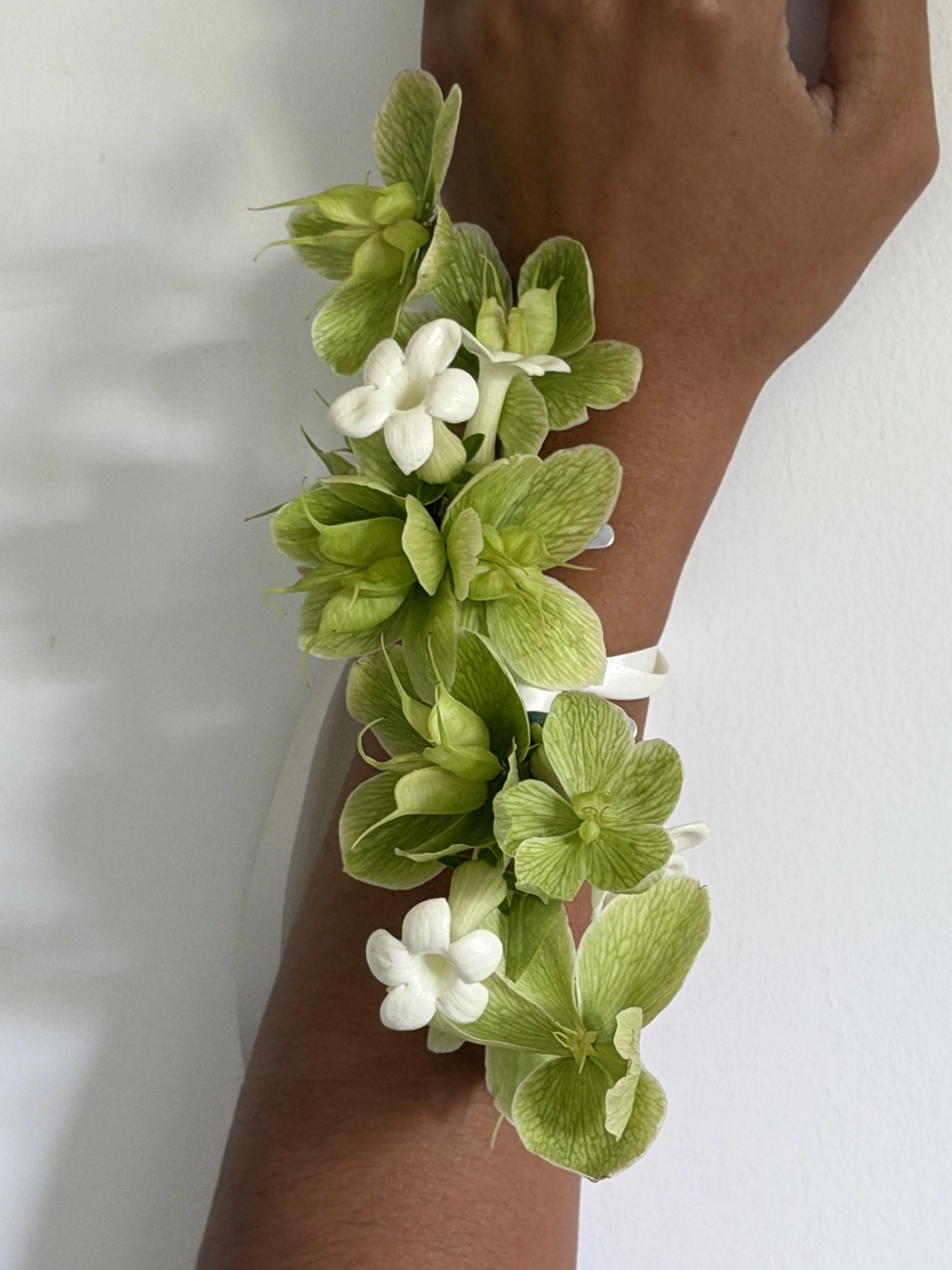 A person's arm wearing a floral corsage made of green hellebores and white jasmine flowers.