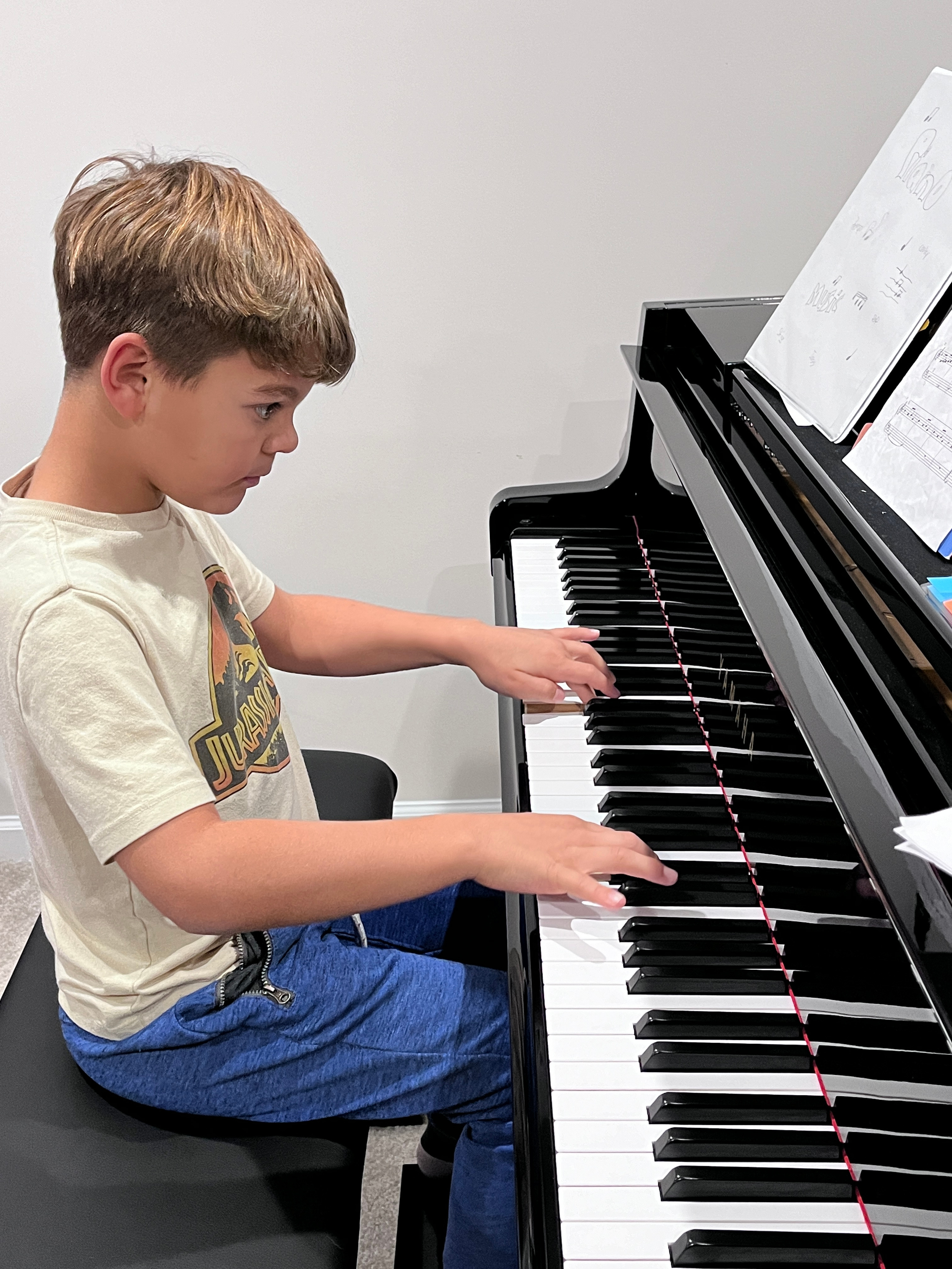 Niño tocando el piano sentado en una banca negra, con partituras sobre el teclado.