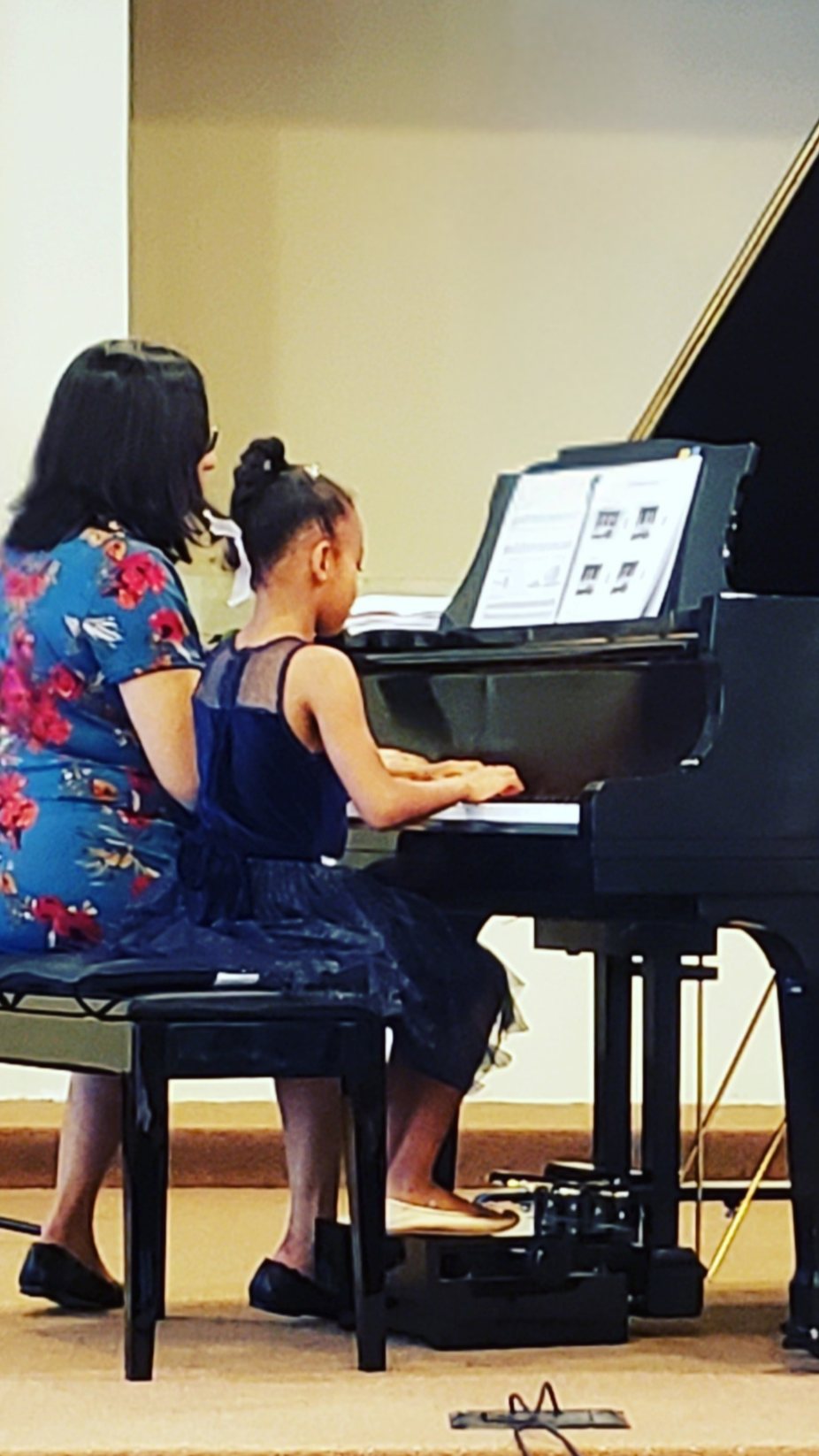 Una mujer y una niña tocando un piano juntos en un recital.