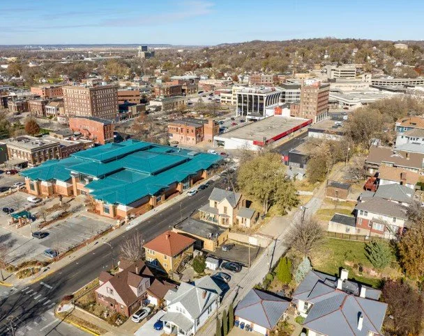 Aerial view of a city neighborhood with a mix of commercial and residential buildings, roads, parking lots, and trees, with a focus on a building with a blue roof.