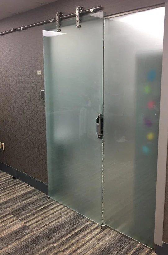 Frosted glass sliding door with track mounted on ceiling, next to textured gray wall and dark patterned carpet.