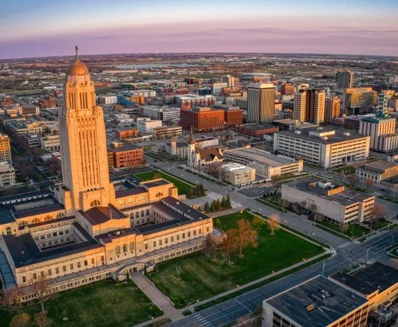 Aerial view of downtown Lincoln, Nebraska, with the Wyoming State Capitol building in the foreground and cityscape extending to the horizon during sunset.