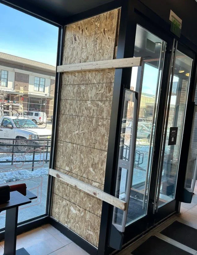 A storefront window with plywood boards and wooden beams blocking the entrance, indicating the store is temporarily closed or under renovation.