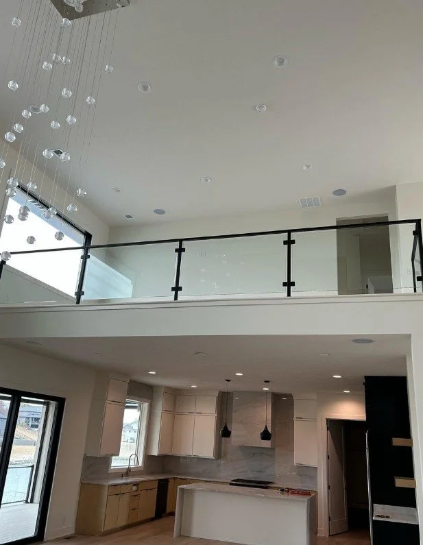 Modern kitchen with white cabinets, marble backsplash, and black pendant lights, open to a high ceiling with a mezzanine level and hanging light fixtures.